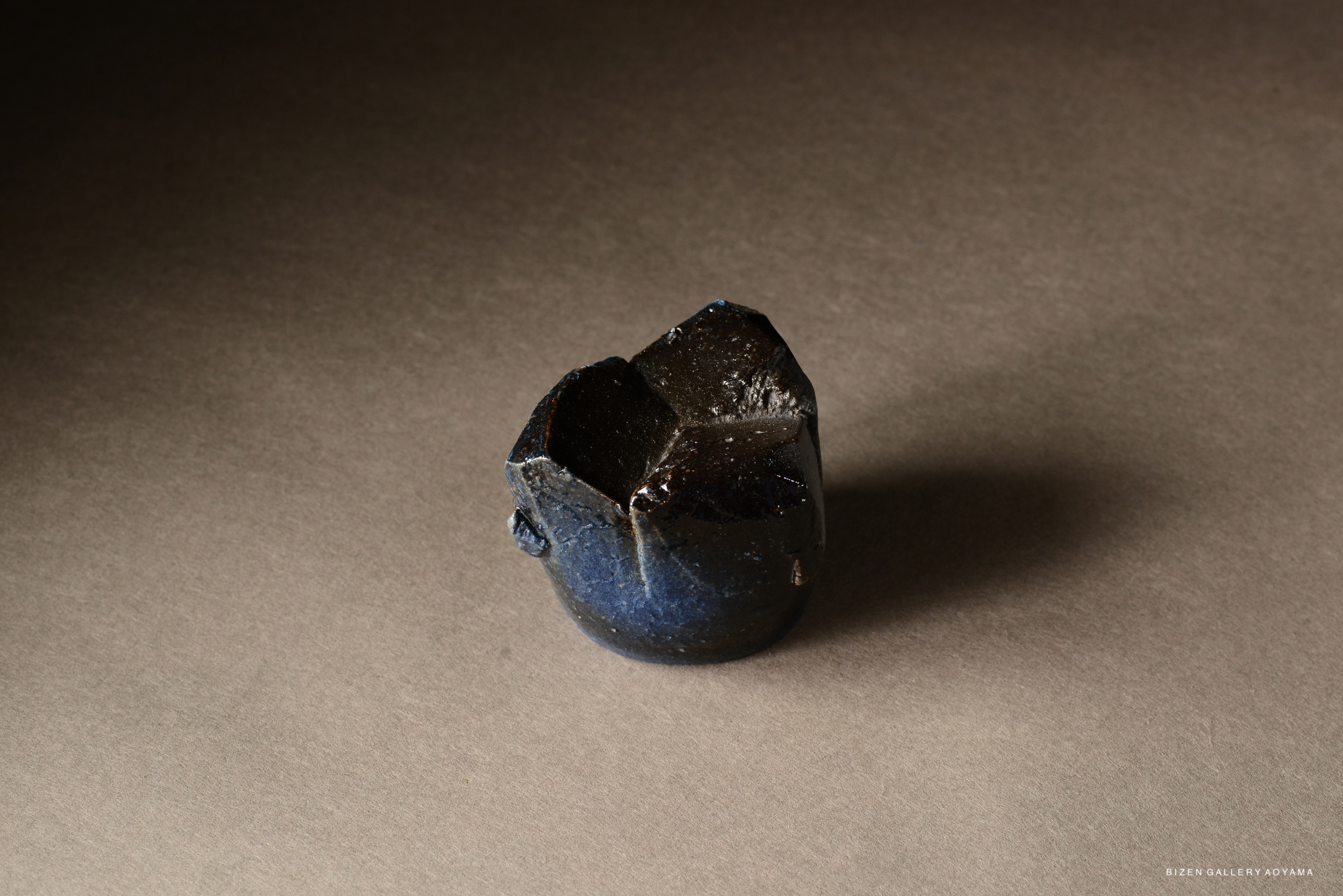 A handcrafted dark ceramic vessel with a unique, irregular shape against a neutral background.