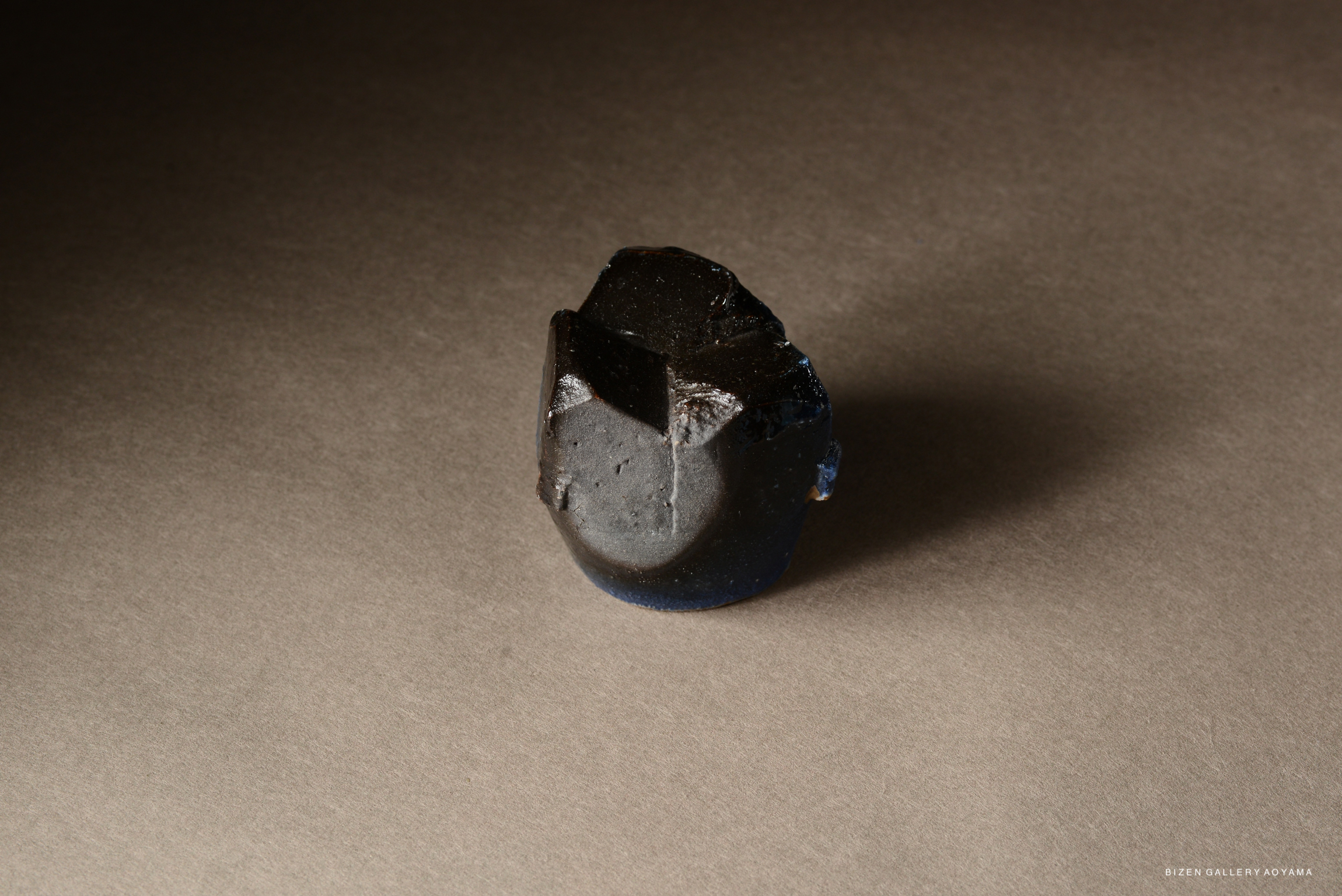 A small, irregularly shaped piece of dark material sits on a gray surface, showcasing its shiny texture and unique contours.