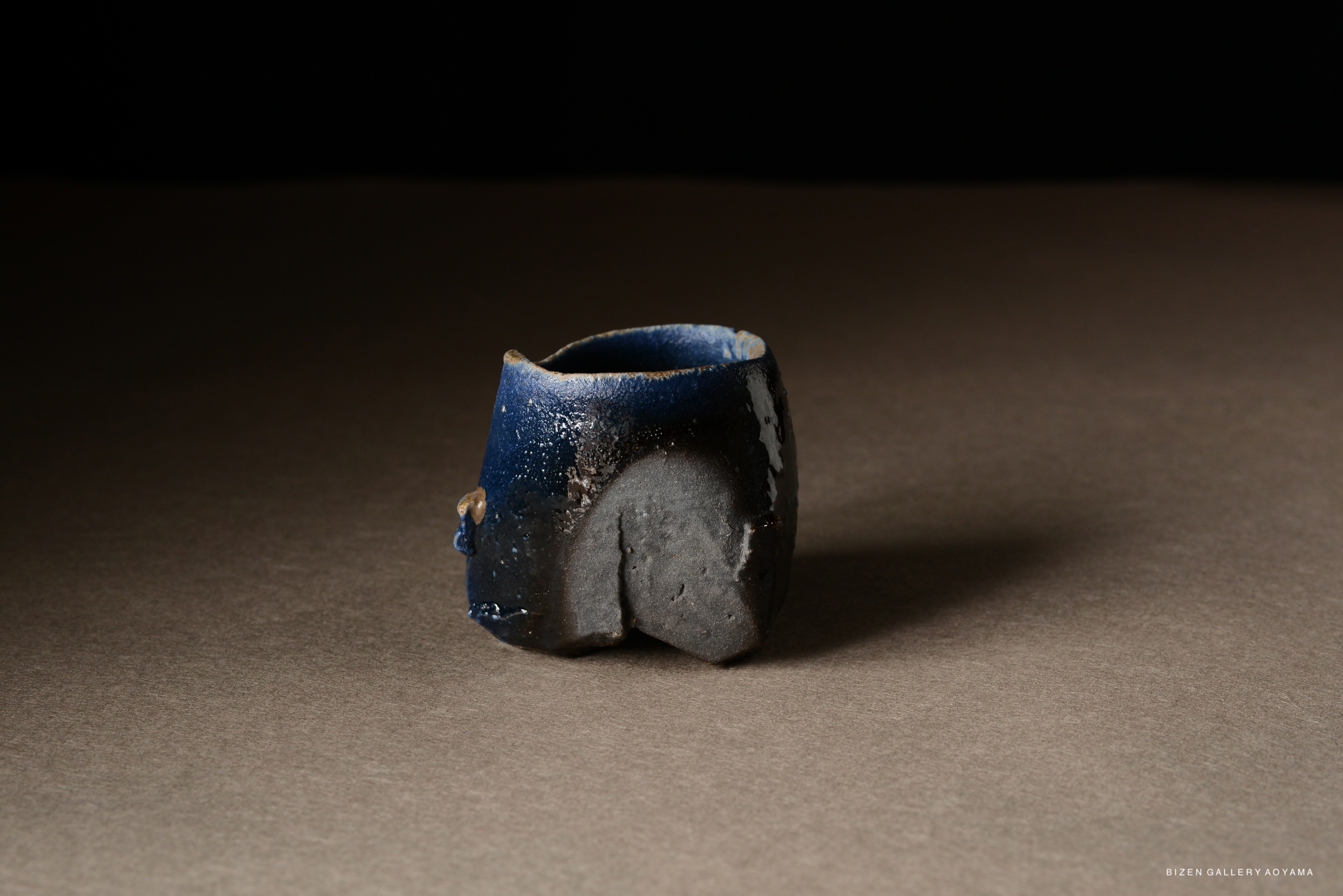 A small ceramic piece with a glossy blue and dark brown finish, set on a neutral surface.