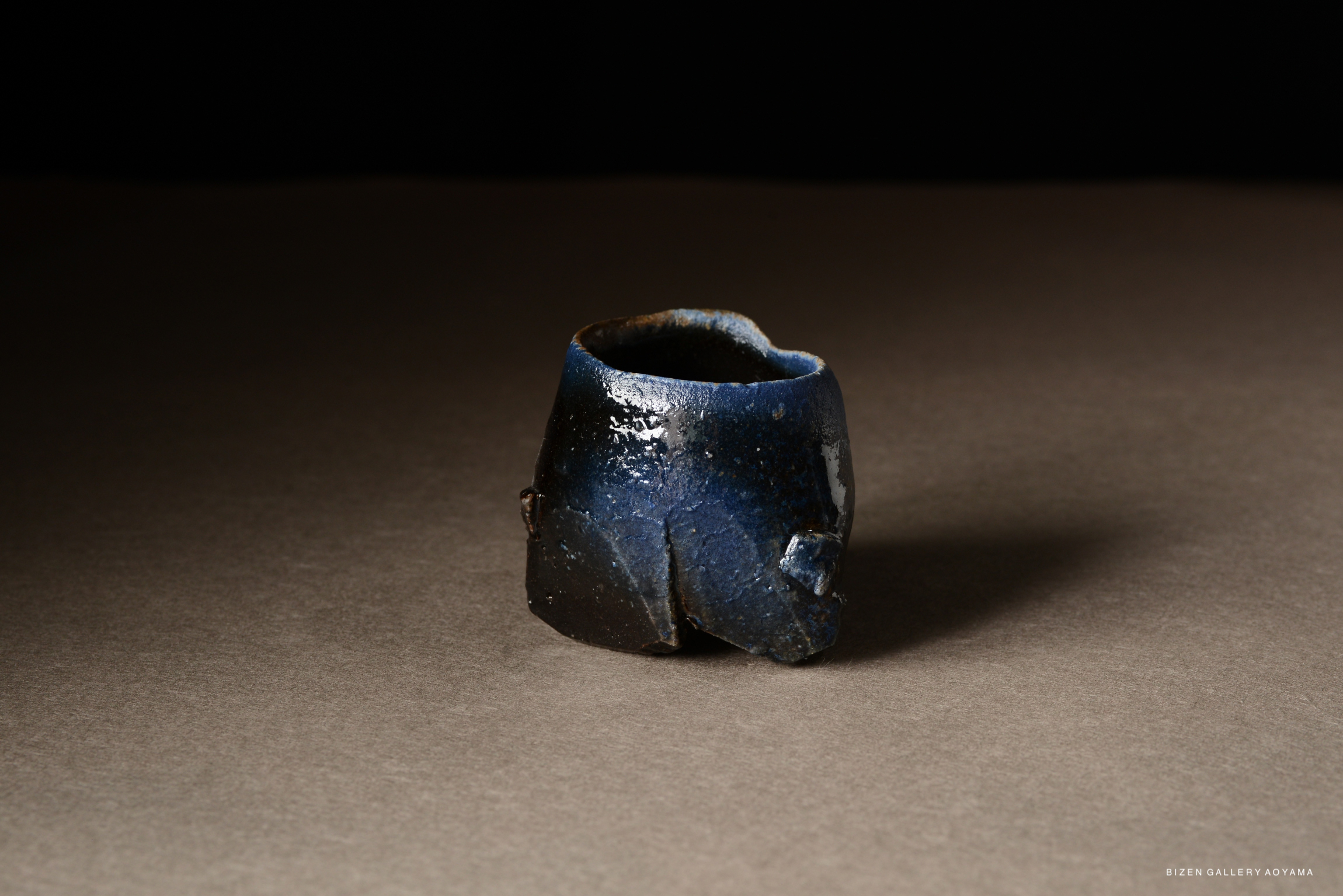 A unique piece of pottery with a dark blue and black exterior, showcasing a rustic and organic shape.