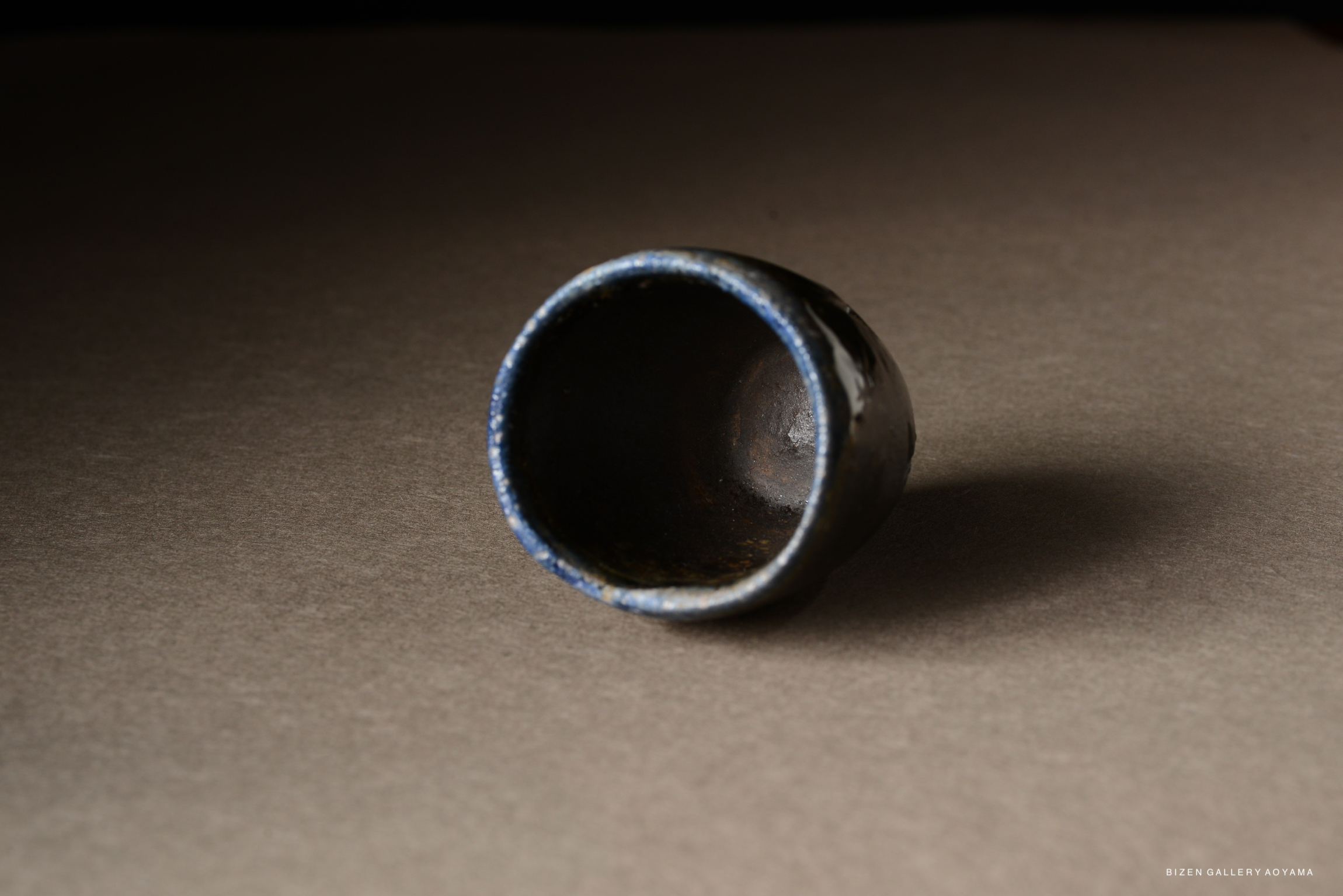 A close-up view of a handcrafted ceramic cup with a dark glaze, resting on a brown surface.