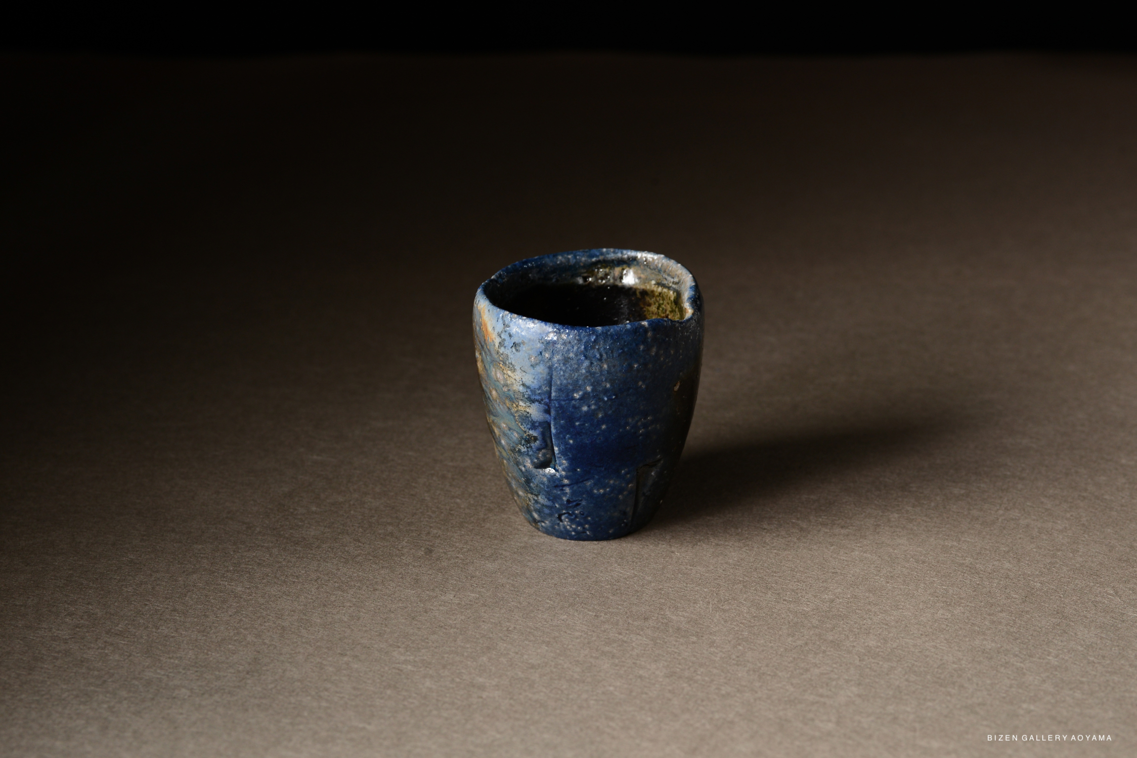 A small blue ceramic cup with a textured surface, placed on a dark background.