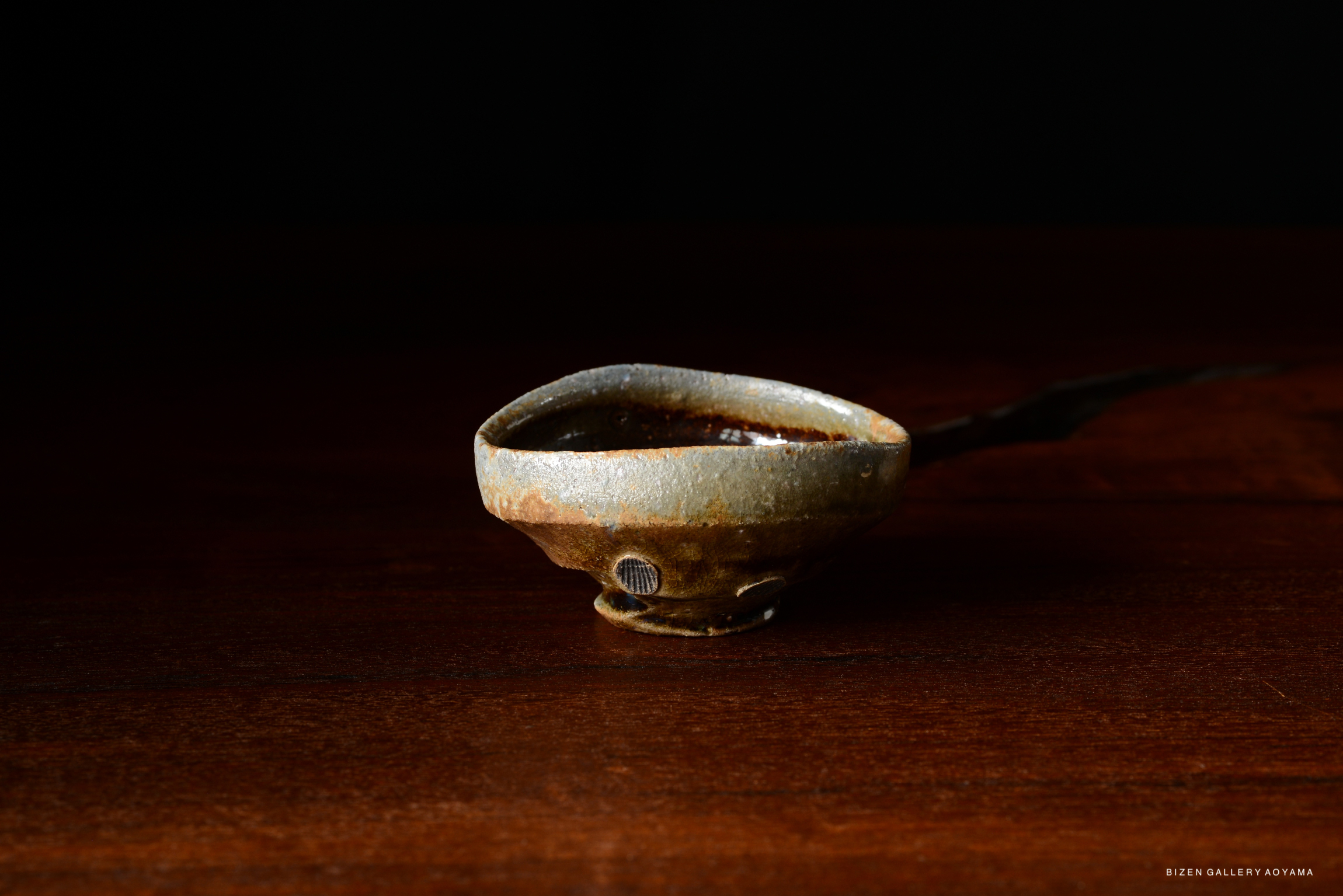 A close-up of a traditional Japanese pottery spoon with a rustic finish, resting on a wooden surface.