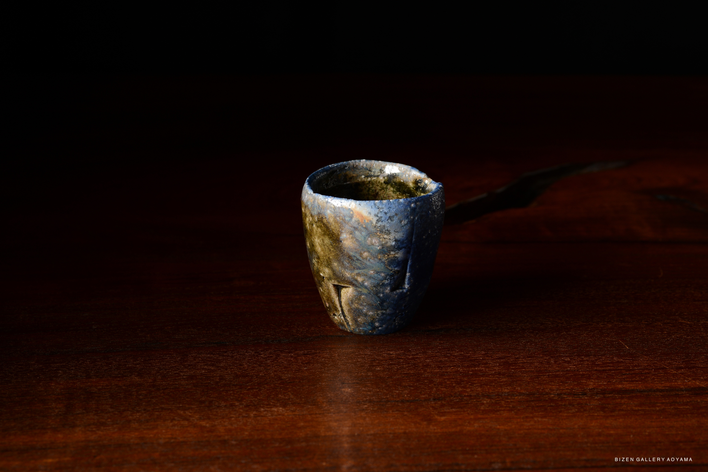 A handcrafted tokkuri (sake vessel) with a unique blue and earthy glaze, displayed on a wooden surface.