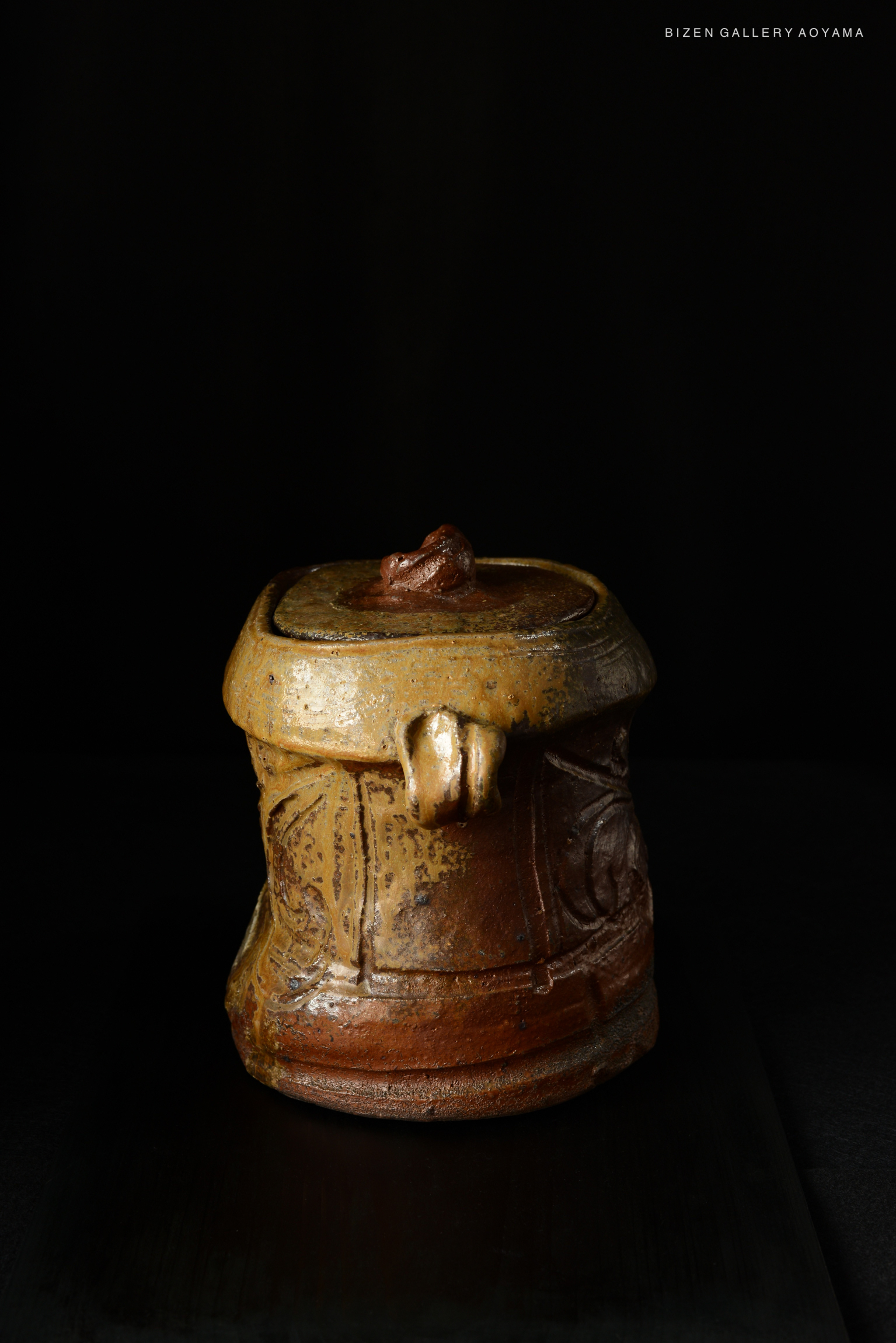 A traditional Bizen Mizusashi with a textured surface, featuring a unique lid design and a rustic color palette, displayed against a black background.