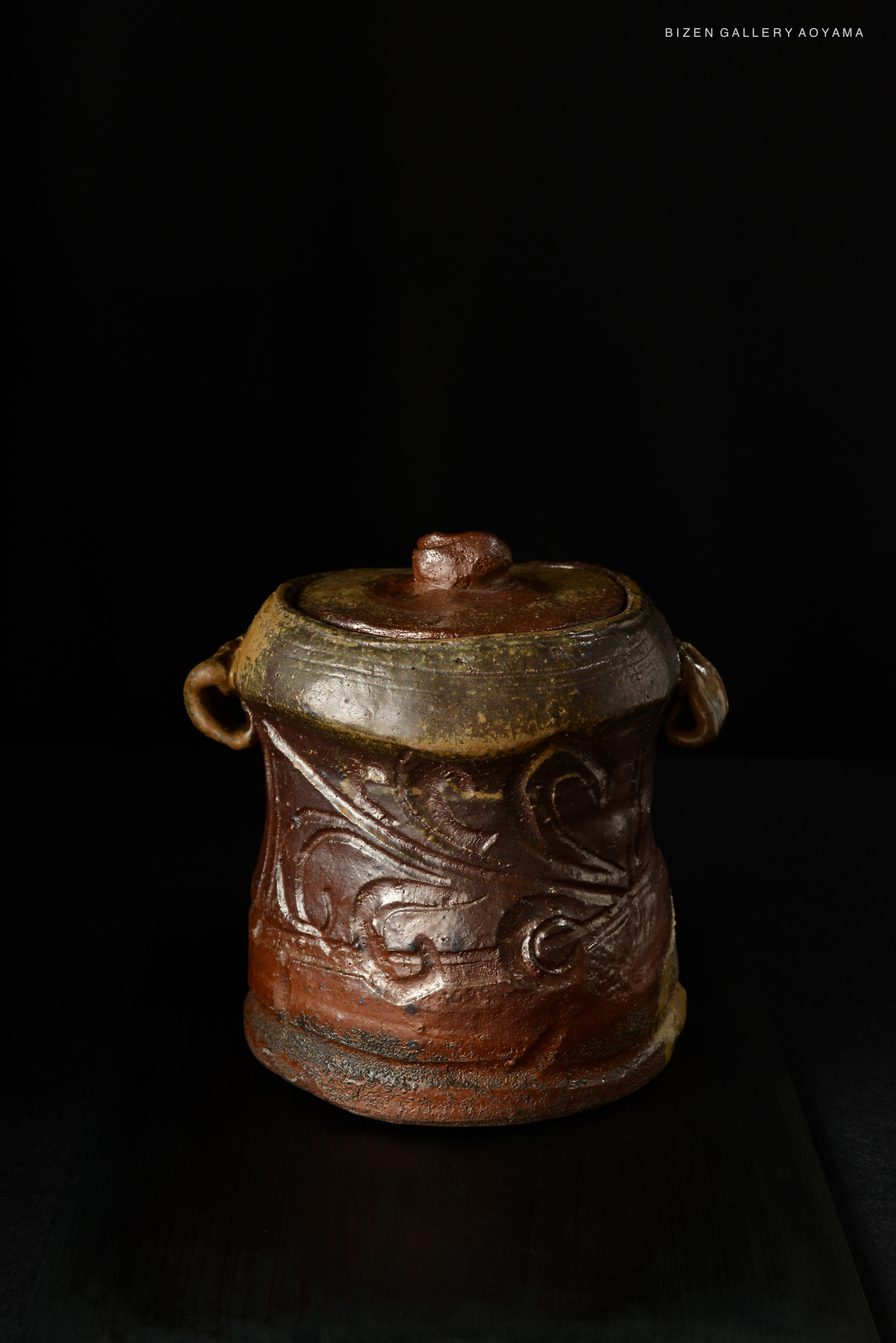 A Bizen Mizusashi ceramic tea container with intricate designs, featuring a rounded shape and a lid on top, displayed against a dark background.
