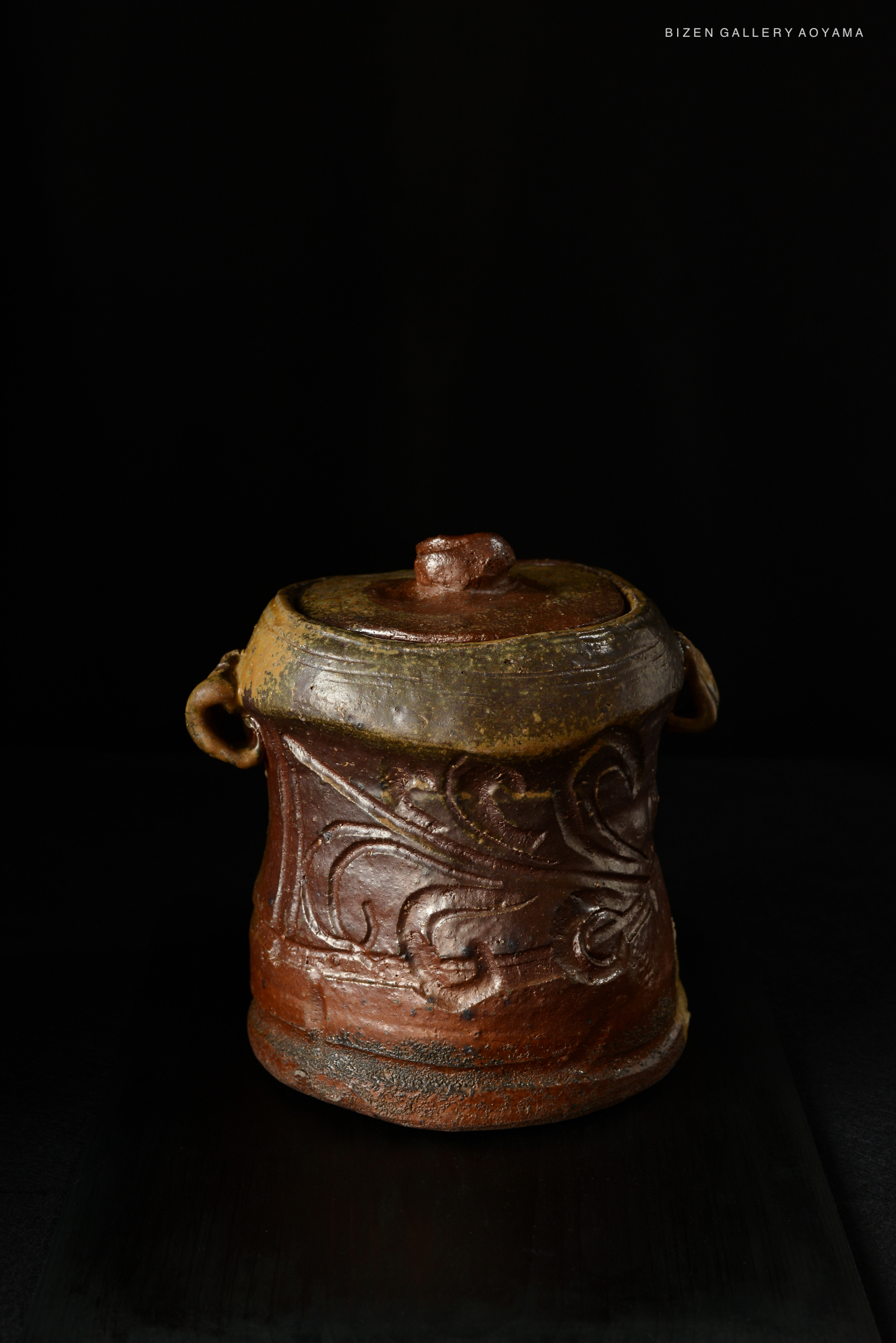 A Bizen Mizusashi (water container) with intricate designs and a natural rustic finish, displayed against a dark background.