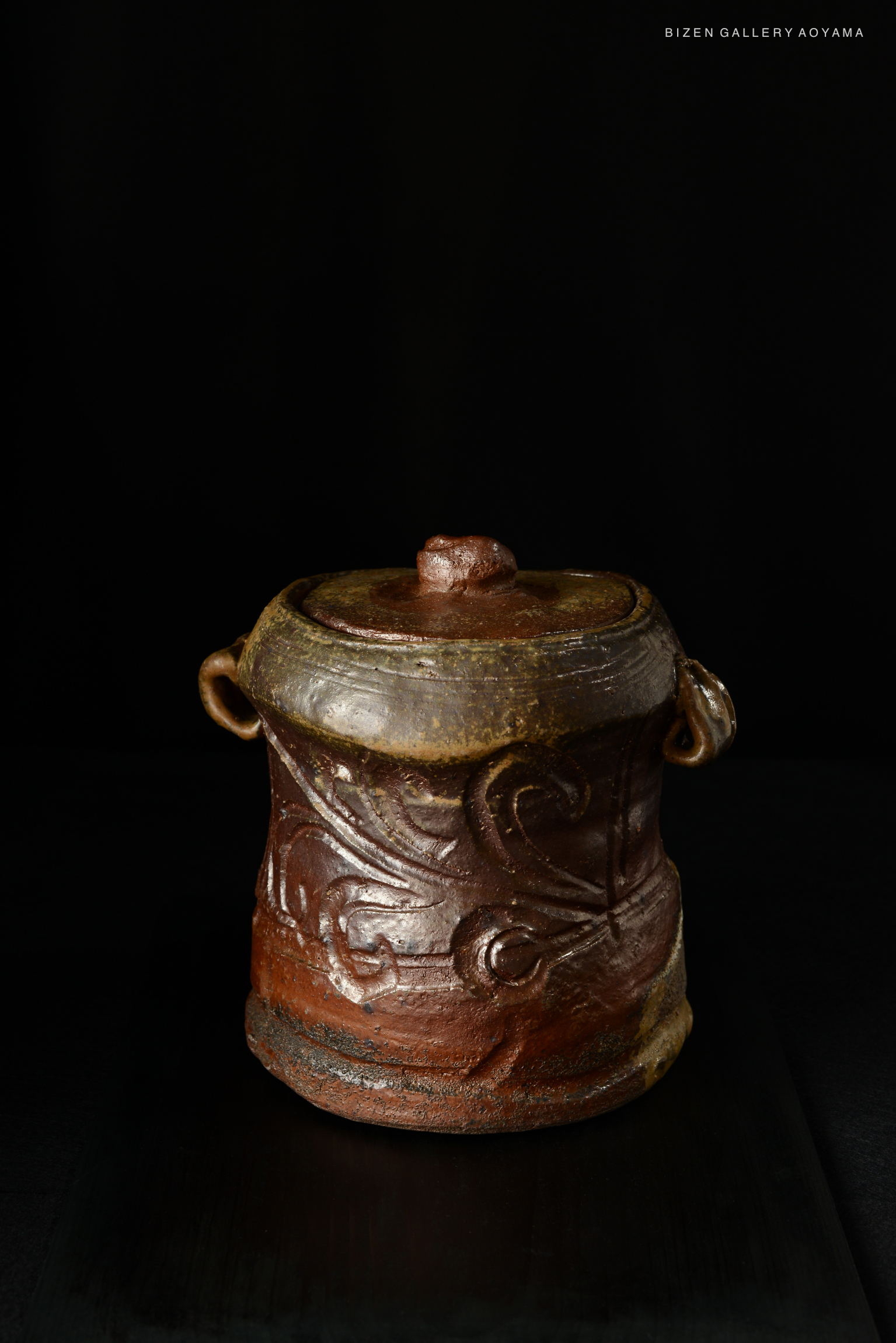 A traditional Bizen Mizusashi teapot with intricate designs and earthy tones, displayed against a dark background.