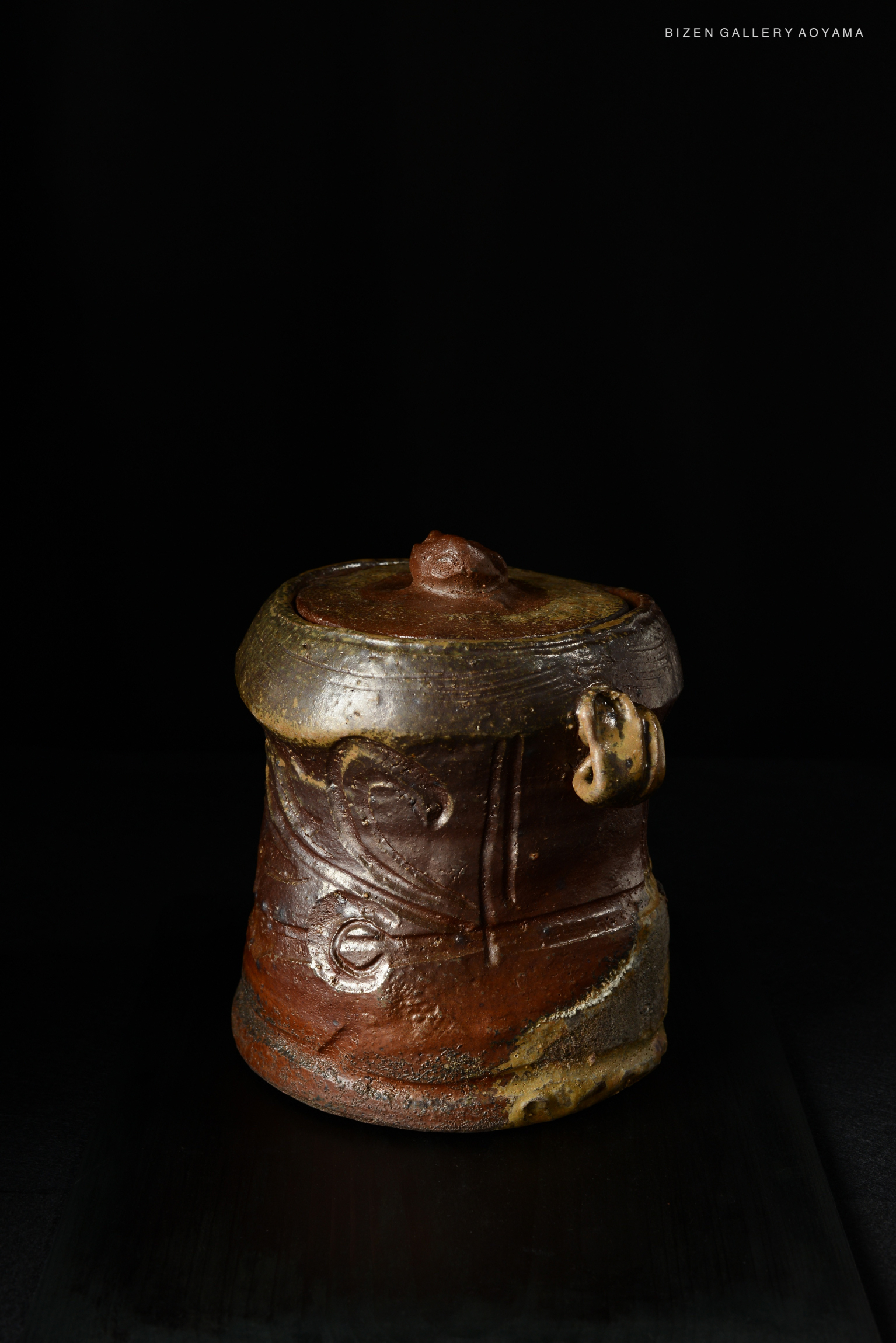 A handcrafted Bizen Mizusashi tea container with intricate designs, showcasing earthy tones and a glossy finish, set against a dark background.
