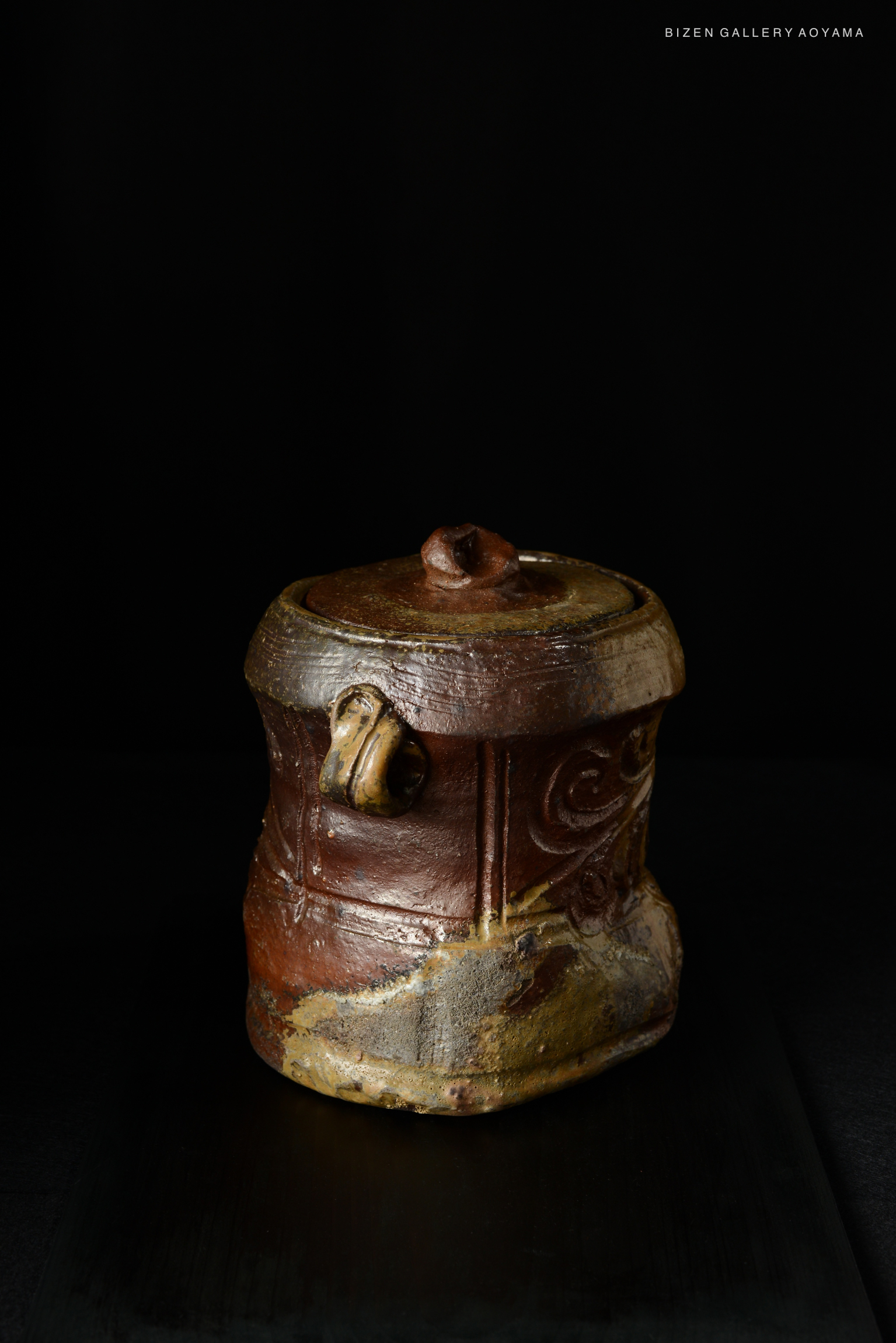 A traditional Bizen Mizusashi with a unique design, featuring earthy colors and intricate surface textures, set against a black background.