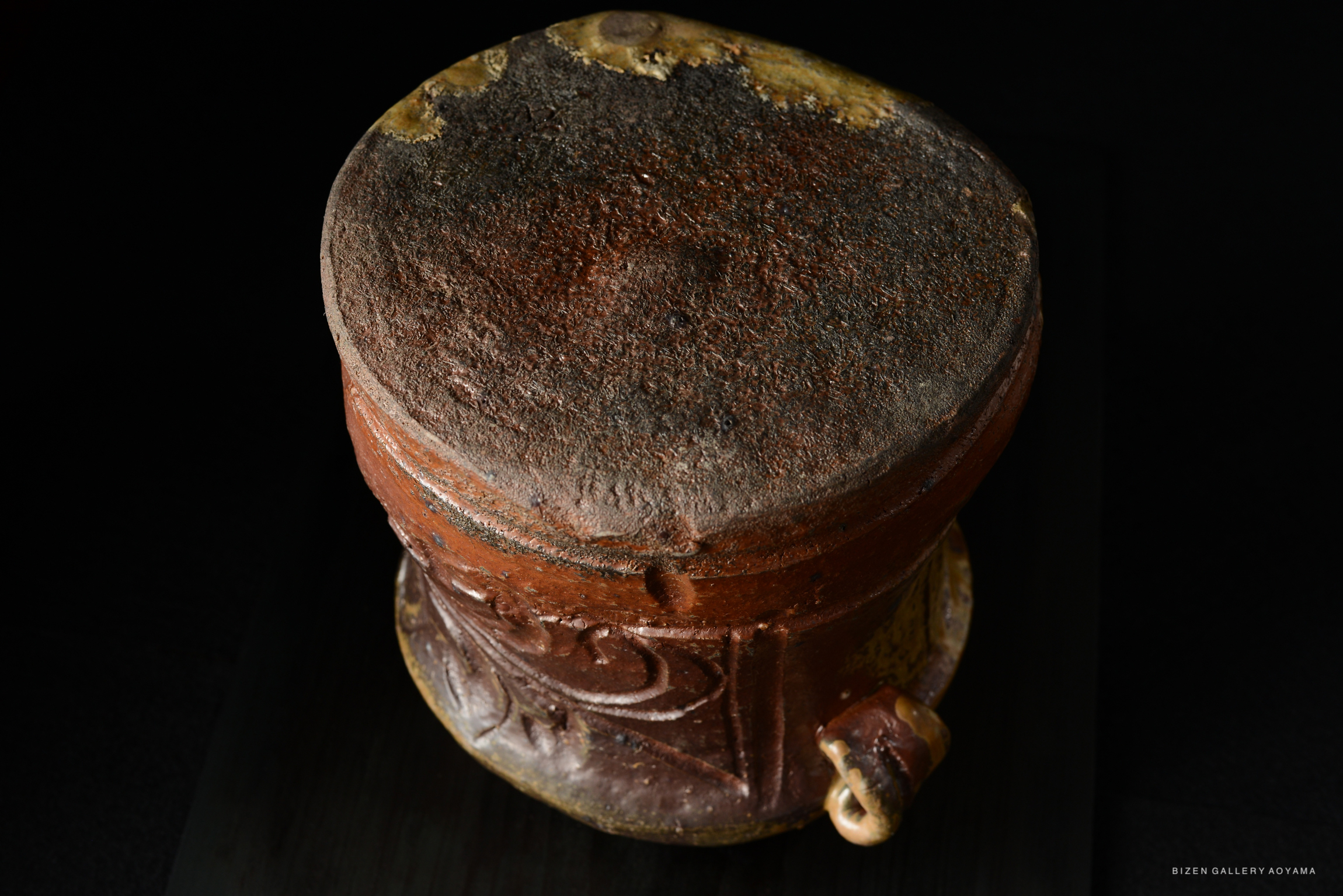 A top view of a traditional Bizen Mizusashi, showcasing its unique texture and colors. The rounded, earthy design features a decorative spout and an intriguing, rustic surface.