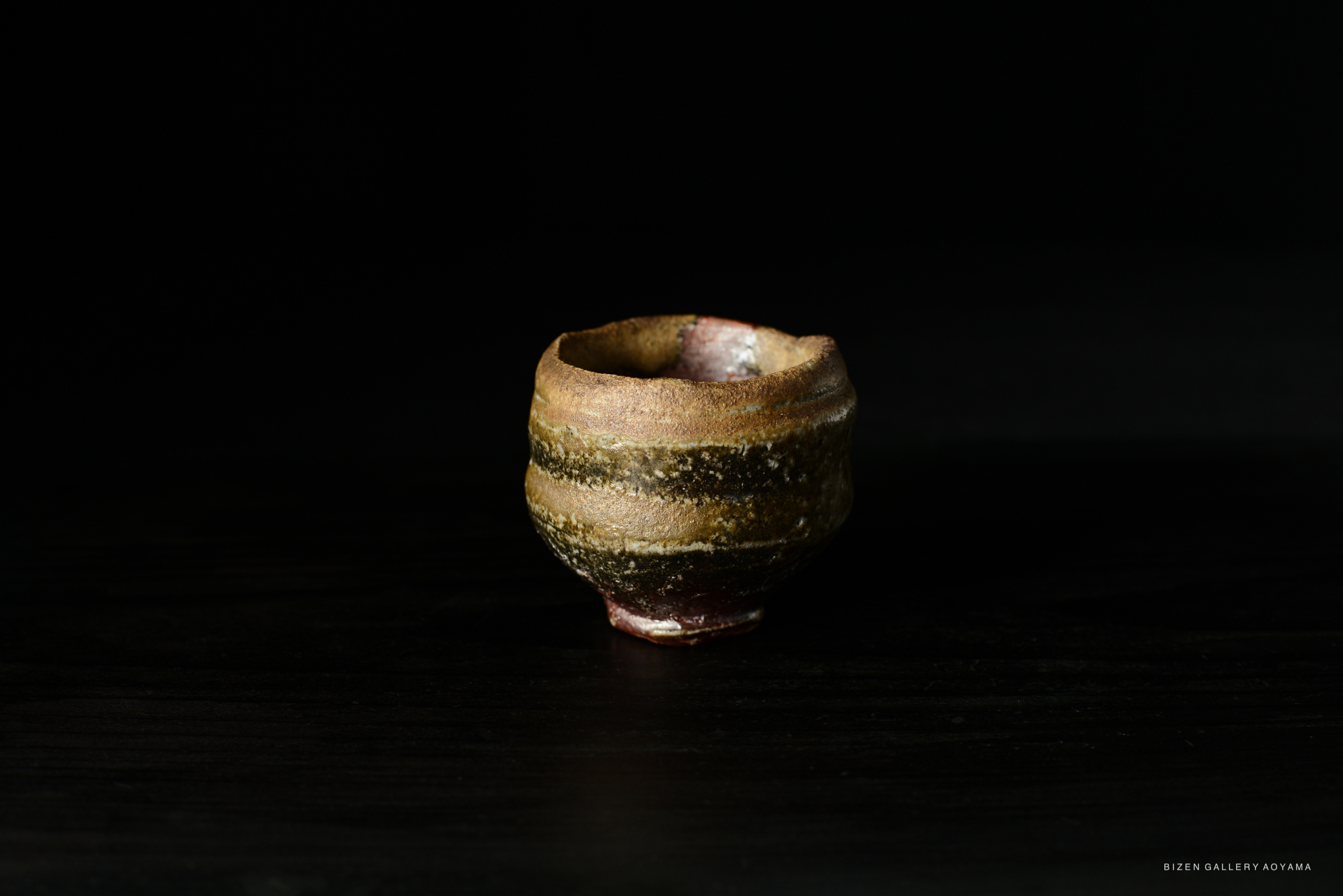 A close-up of a Bizen Guinomi sake cup with a textured finish, showcasing earthy colors and a unique shape.