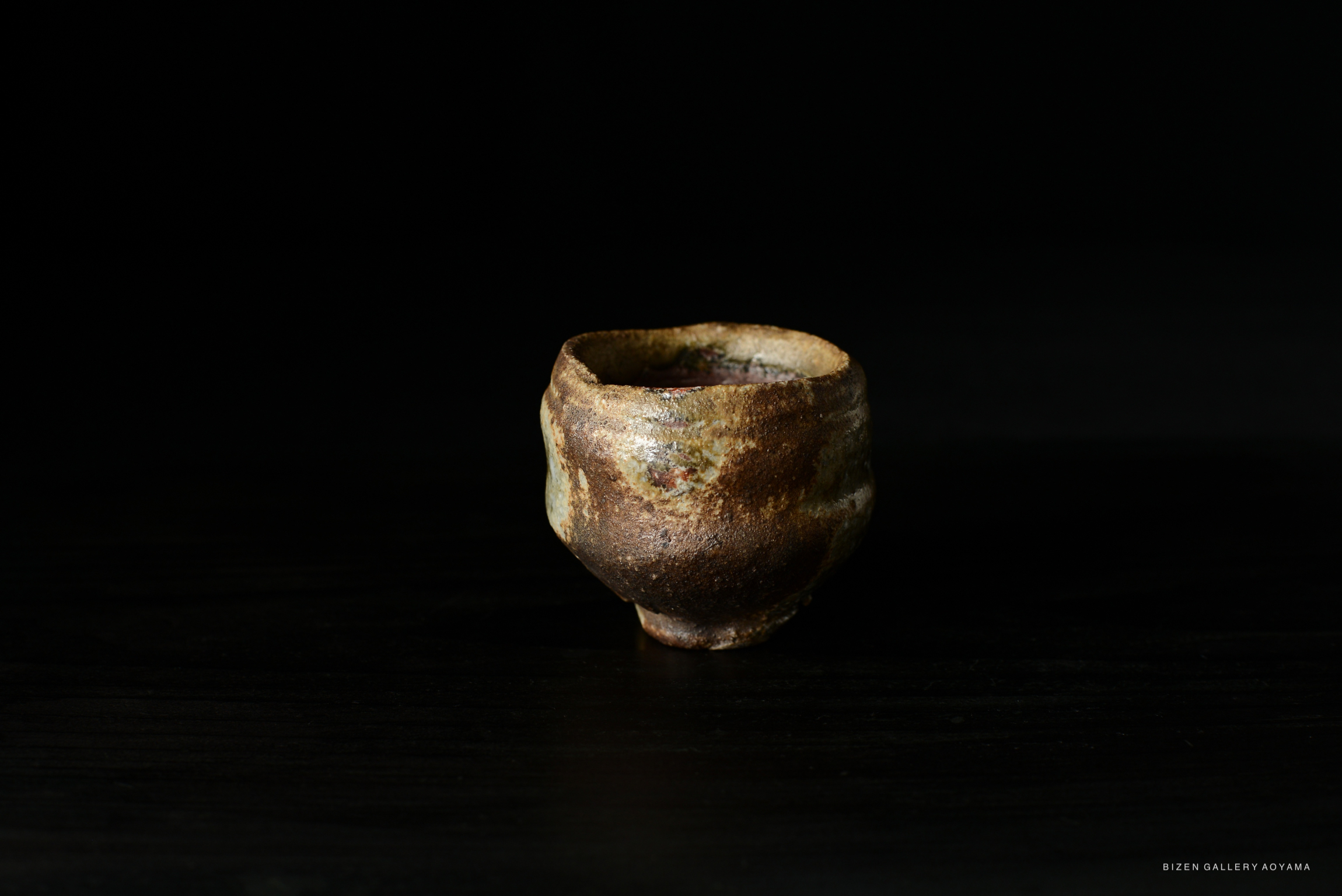 A small, rustic ceramic pot with earthy tones, placed on a dark background.