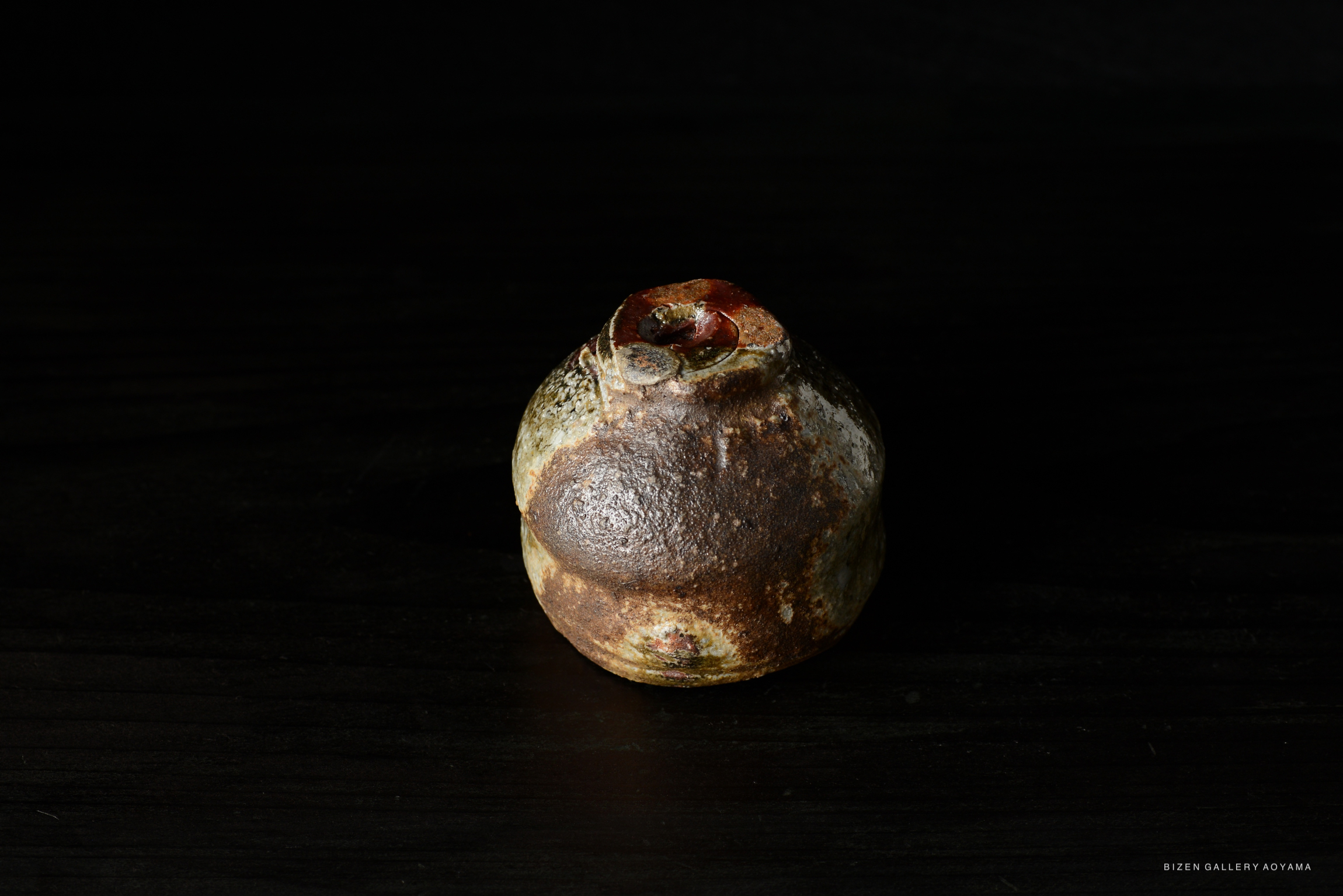 A close-up view of a Bizen Guinomi sake cup, showcasing its unique texture and color, set against a dark background.