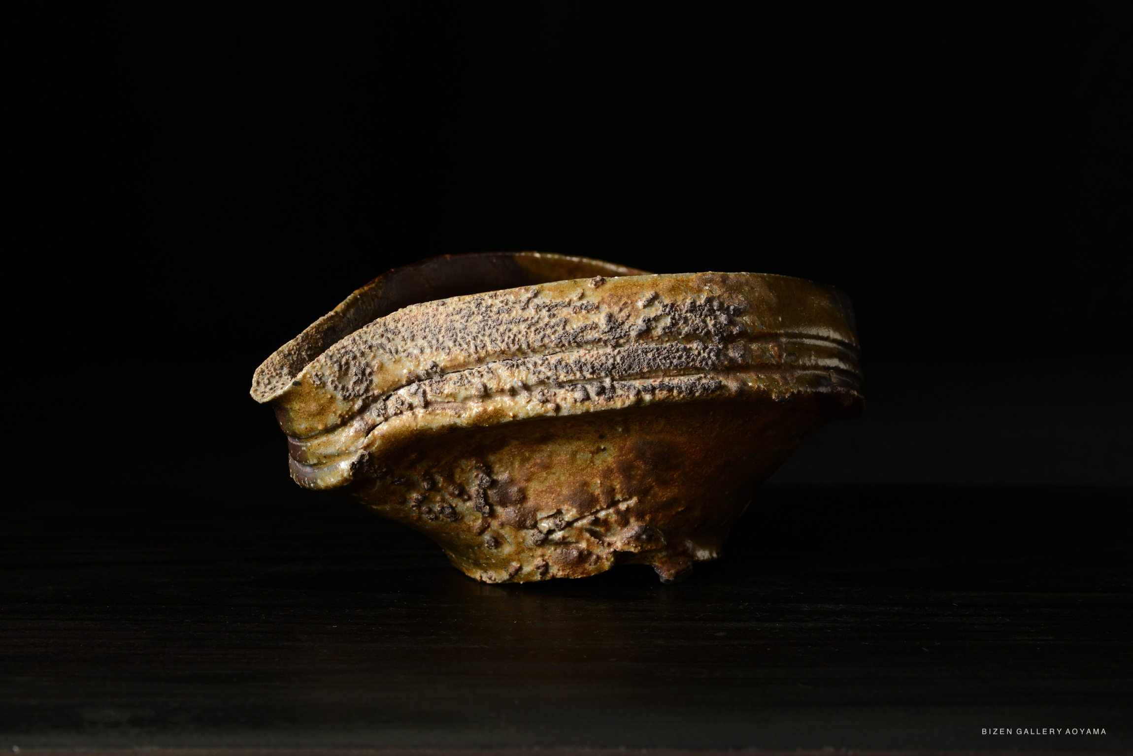 A Bizen-style Guinomi, showcasing a unique textured surface and organic shape, displayed against a dark backdrop.