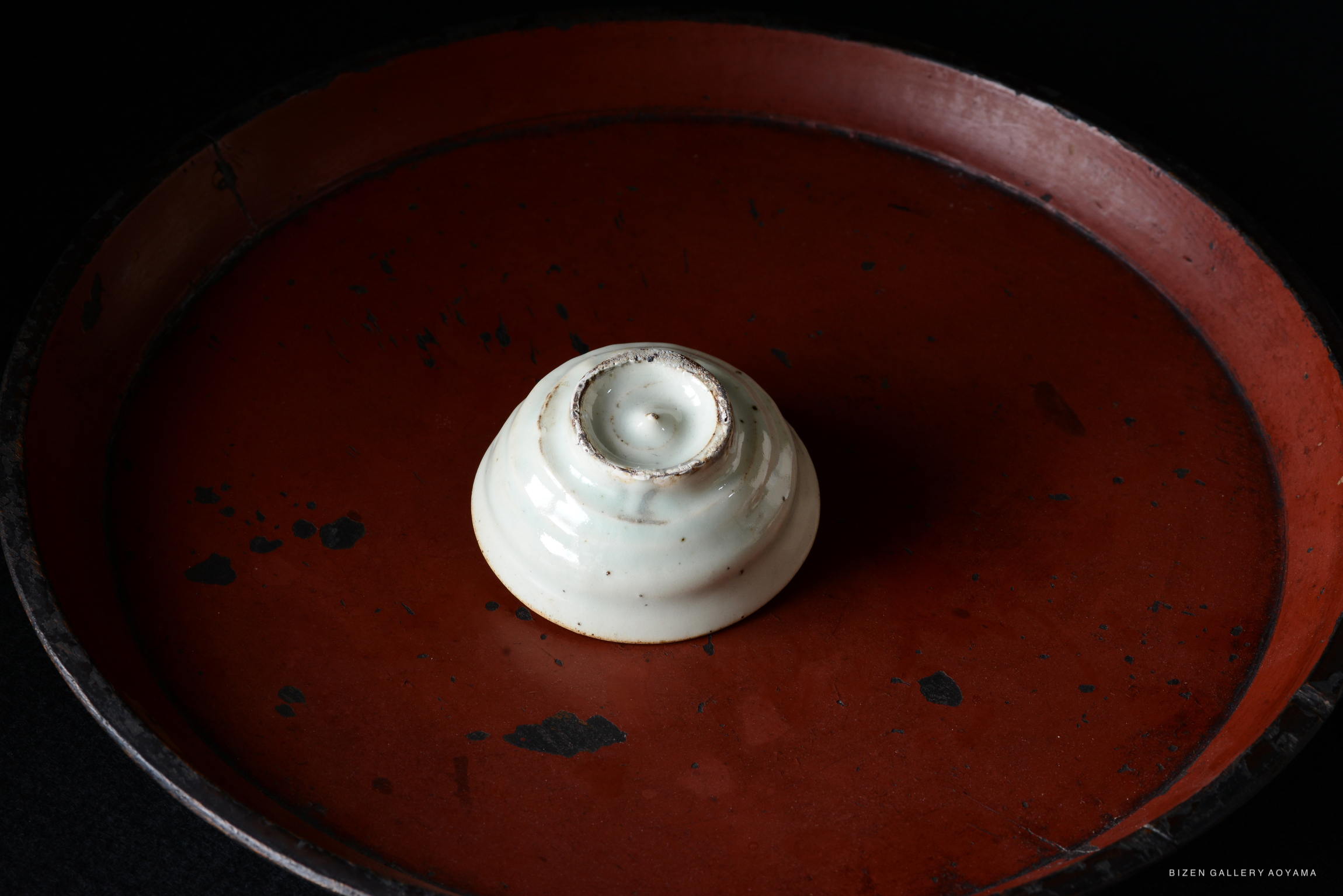 A small, white ceramic piece placed on a round, reddish-brown tray with a dark background.