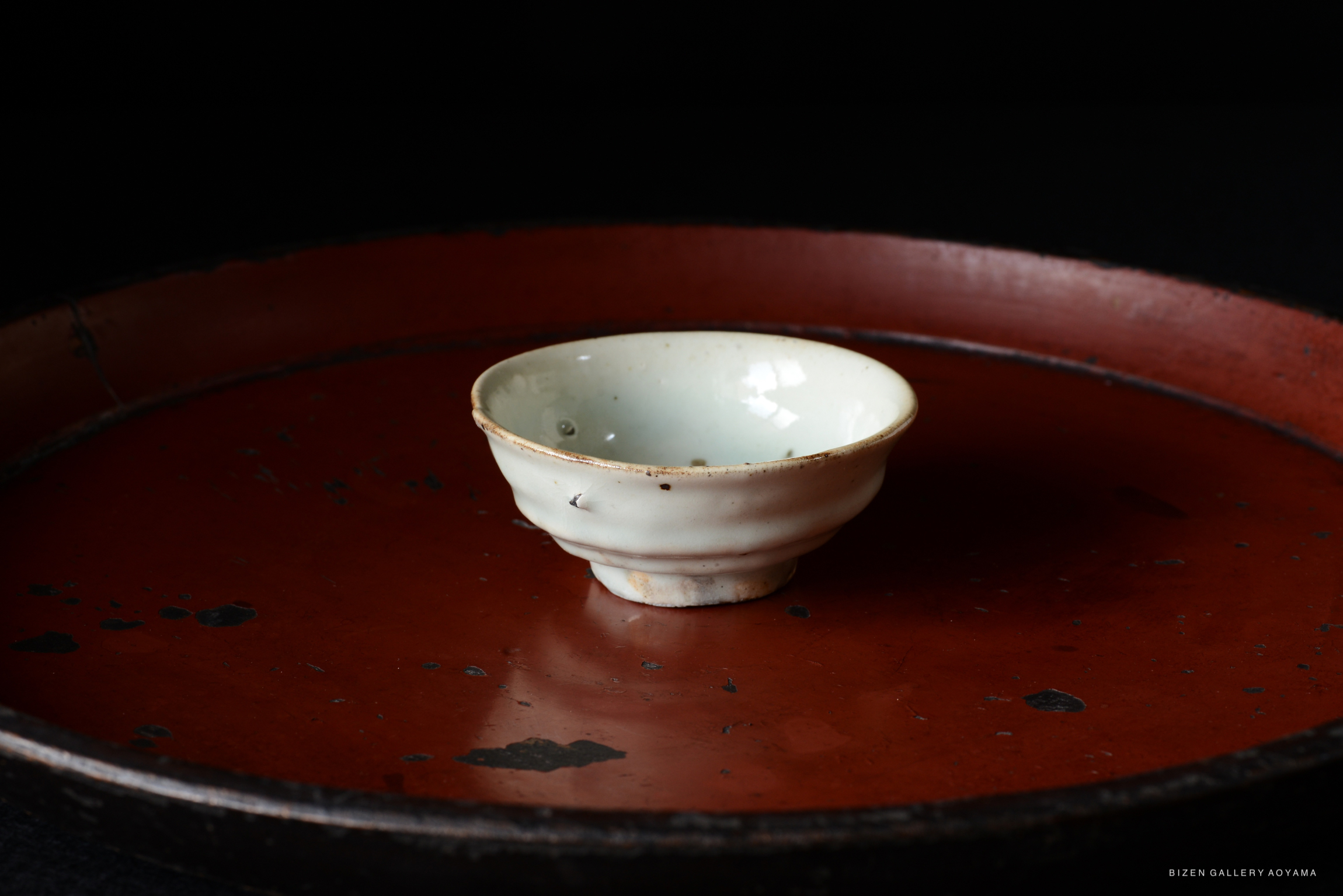 A small, white ceramic bowl resting on a round, red tray with visible wear and marks.