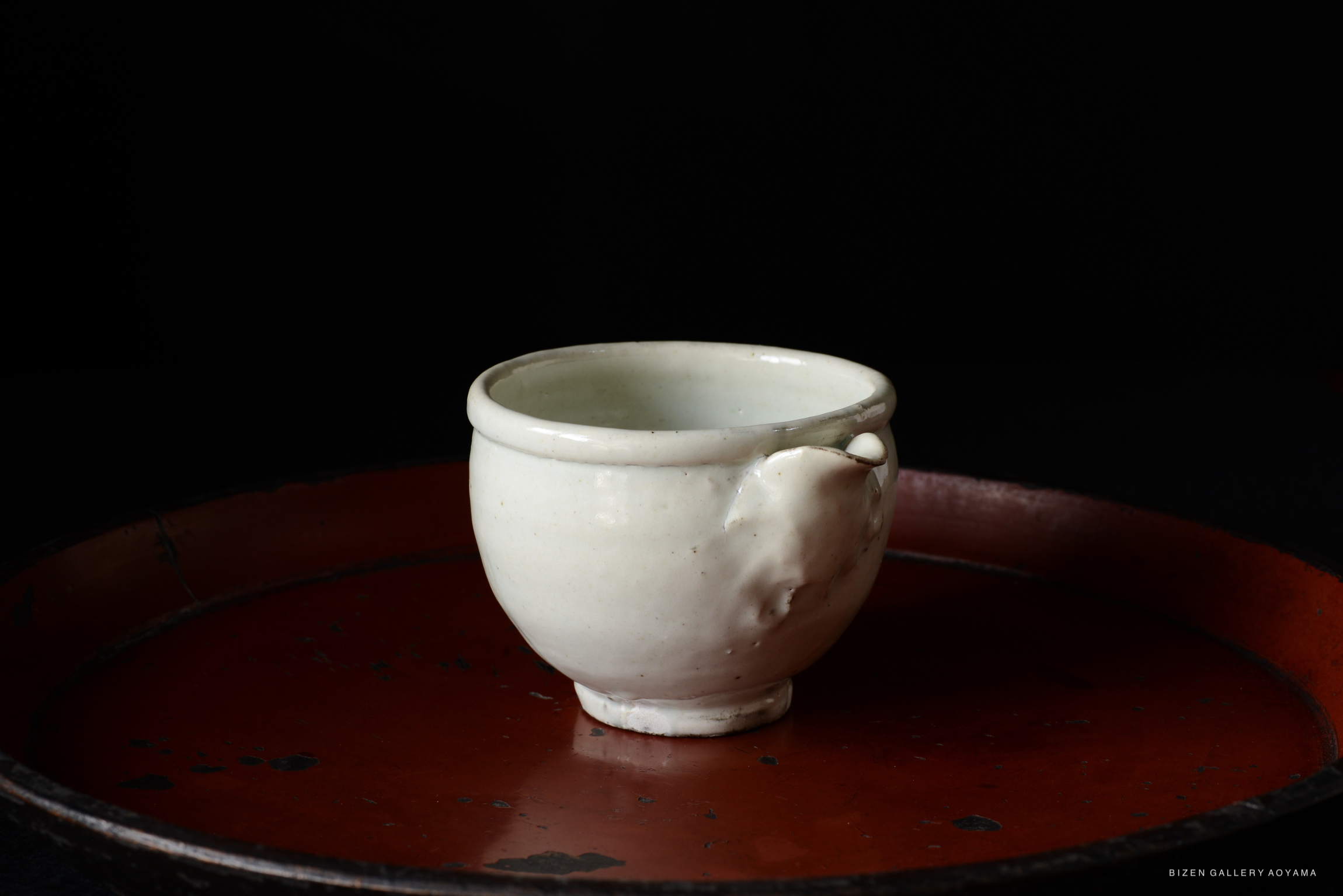 A simple white ceramic cup with a small handle, placed on a round, red tray against a black background.