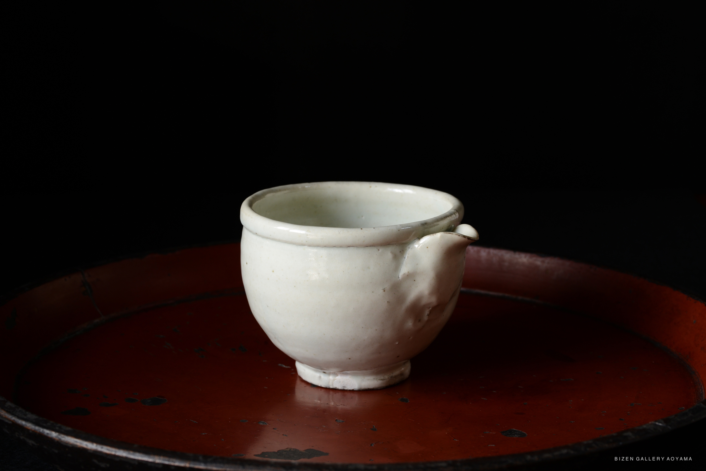 A white ceramic cup with a handle, placed on a circular red tray against a dark background.