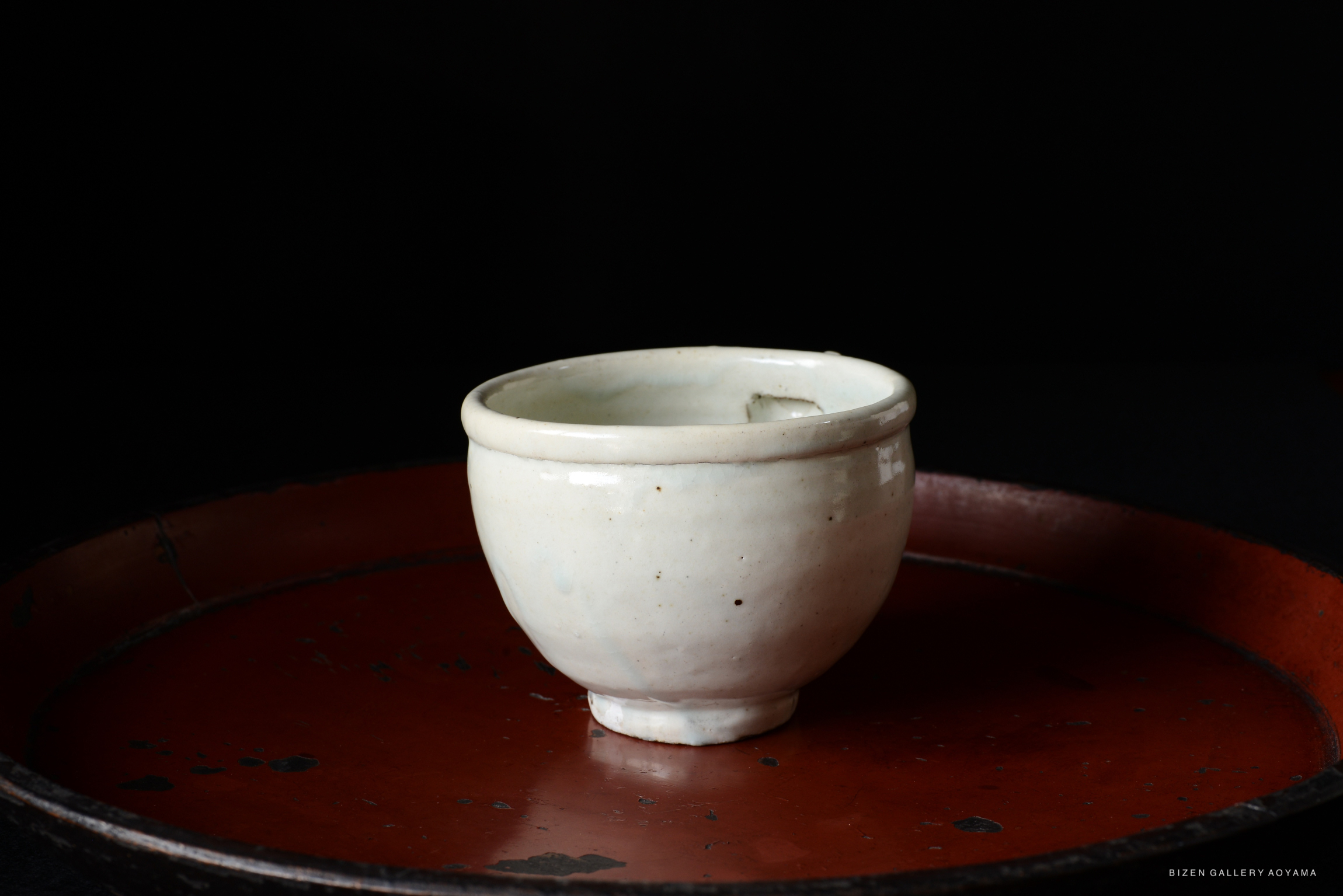 A close-up view of a small white ceramic cup placed on a round red tray, with a dark background.