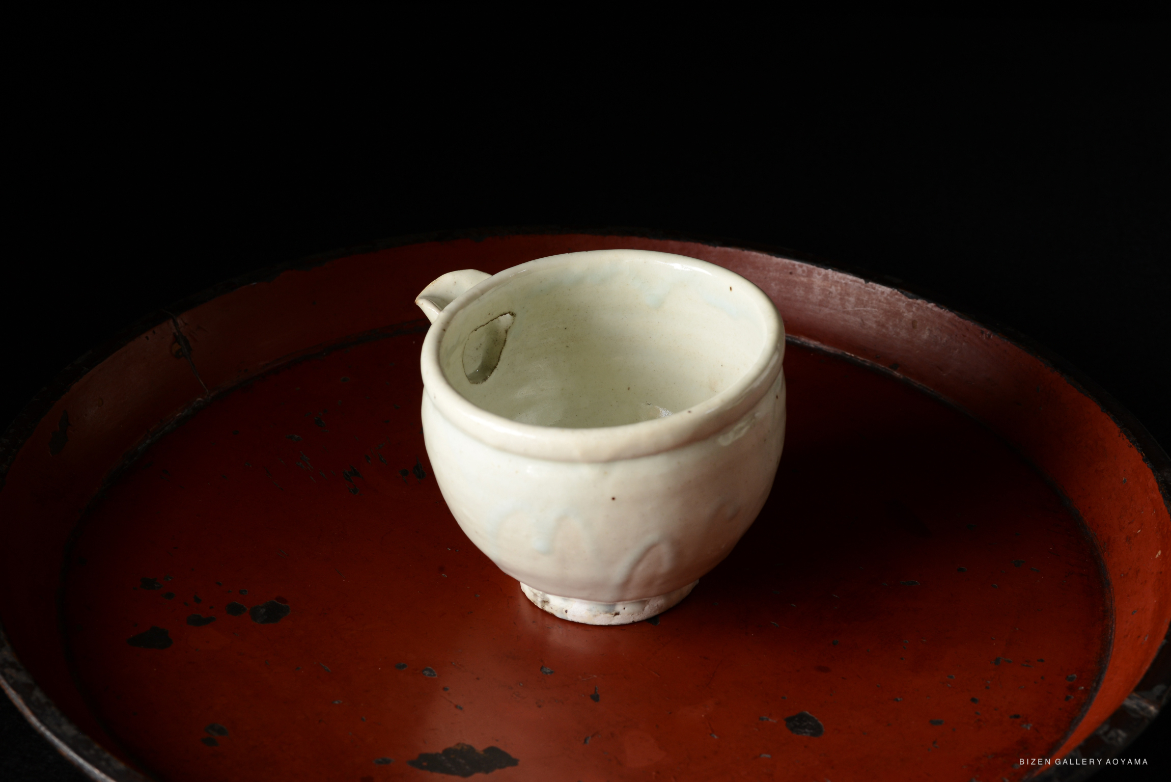 A ceramic cup with a small handle, placed on a round red tray, against a black background.