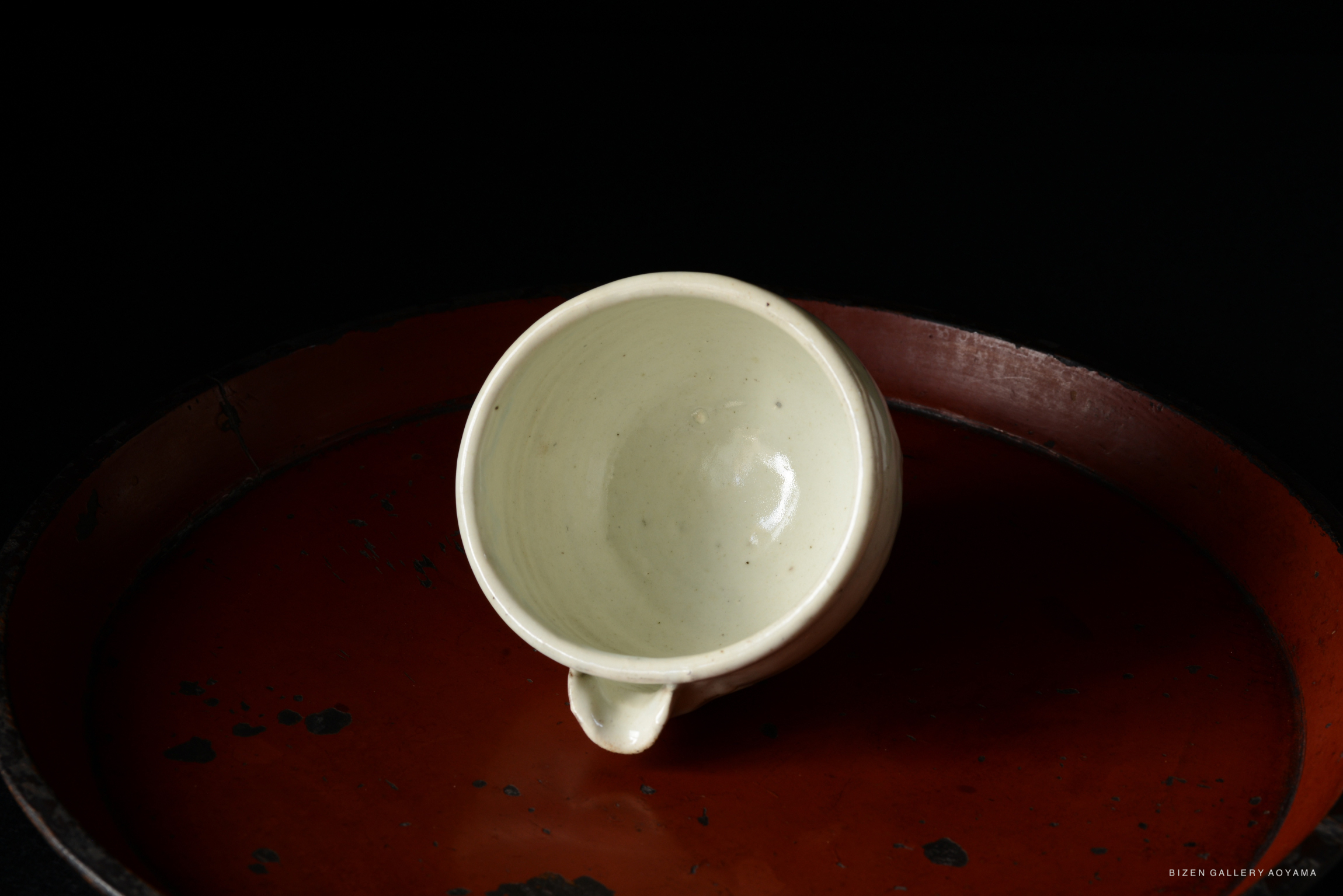 A small white ceramic cup placed on a red lacquer tray, against a black background.
