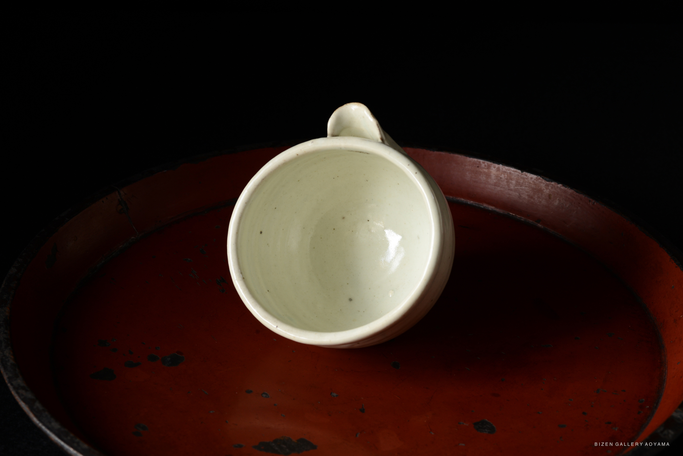 Close-up view of a white ceramic cup on a red lacquer plate, set against a black background.
