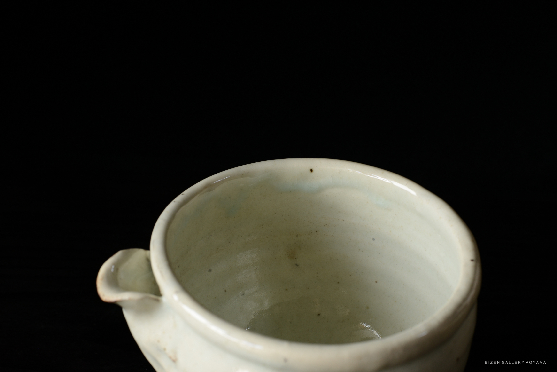 Close-up view of a light-colored ceramic bowl with a small handle, set against a black background.