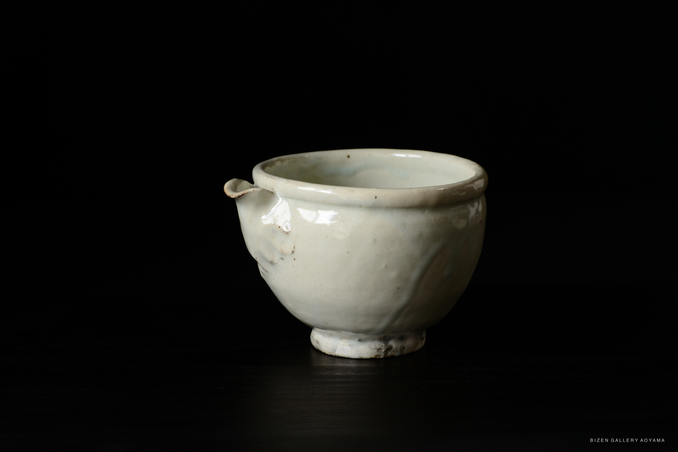 A small, cream-colored ceramic bowl with a slightly curved rim and a pedestal base, set against a black background.