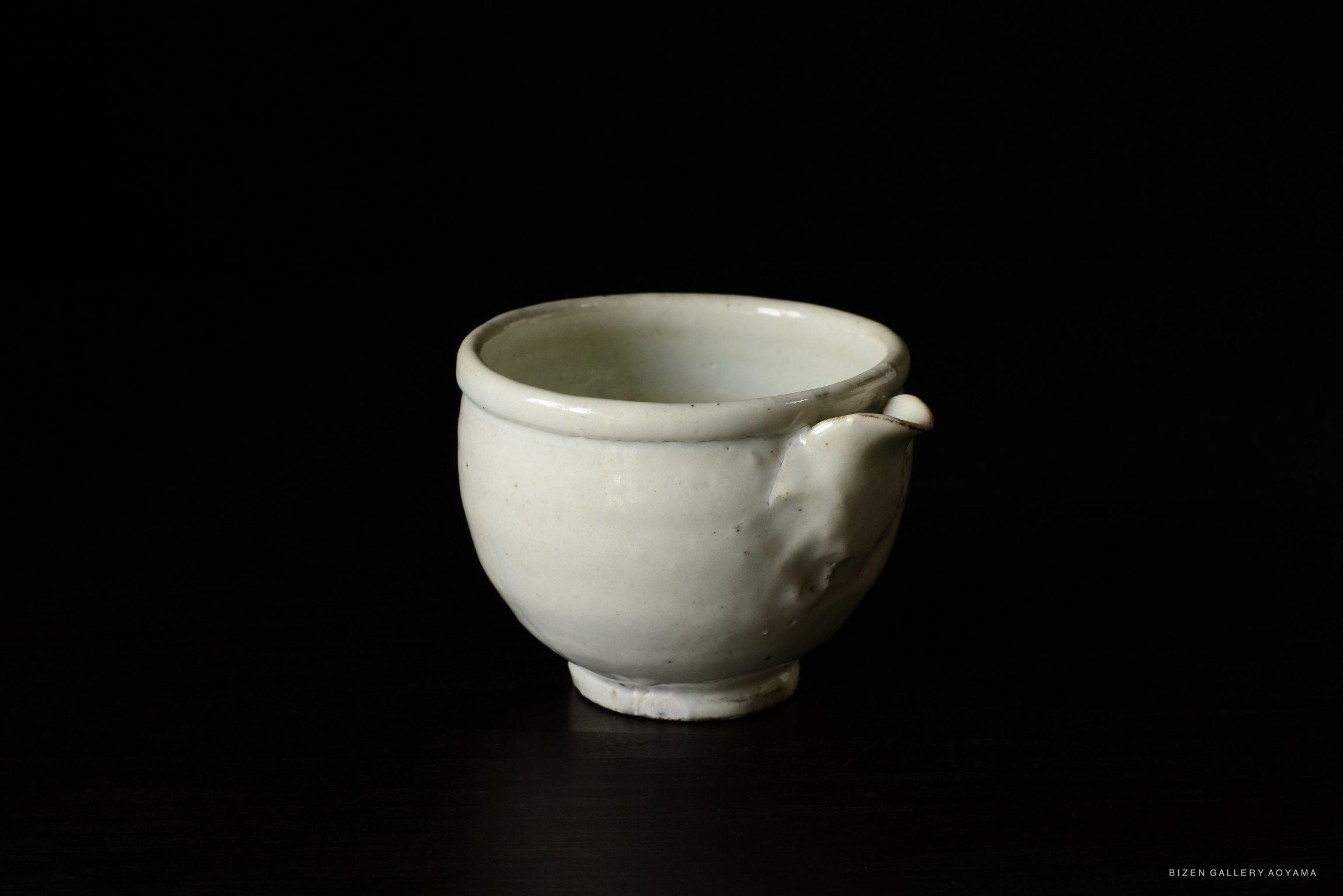 A white ceramic cup with a spout, set against a black background.