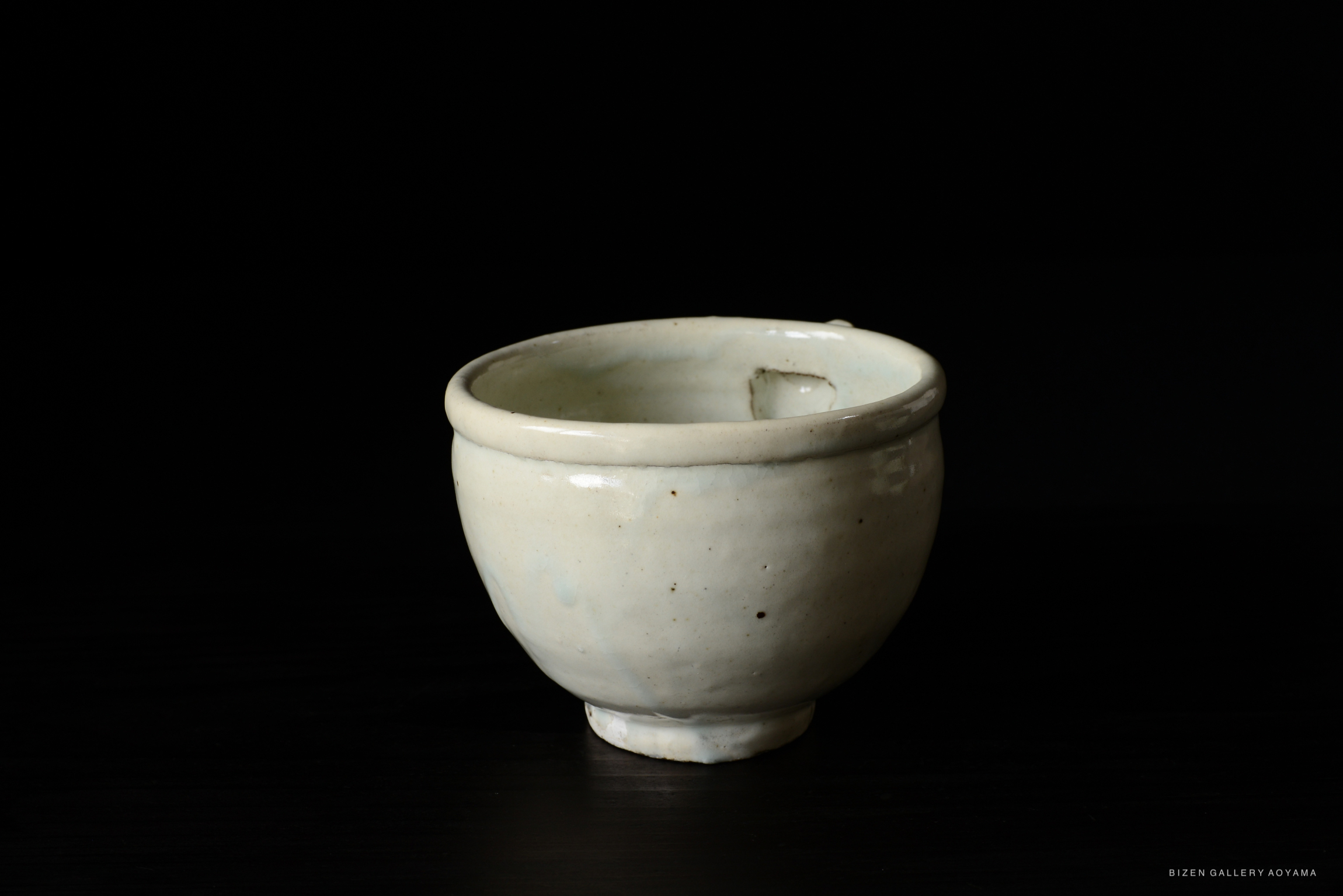 A small, round white ceramic bowl with a smooth surface and a slight indentation, placed on a dark background.