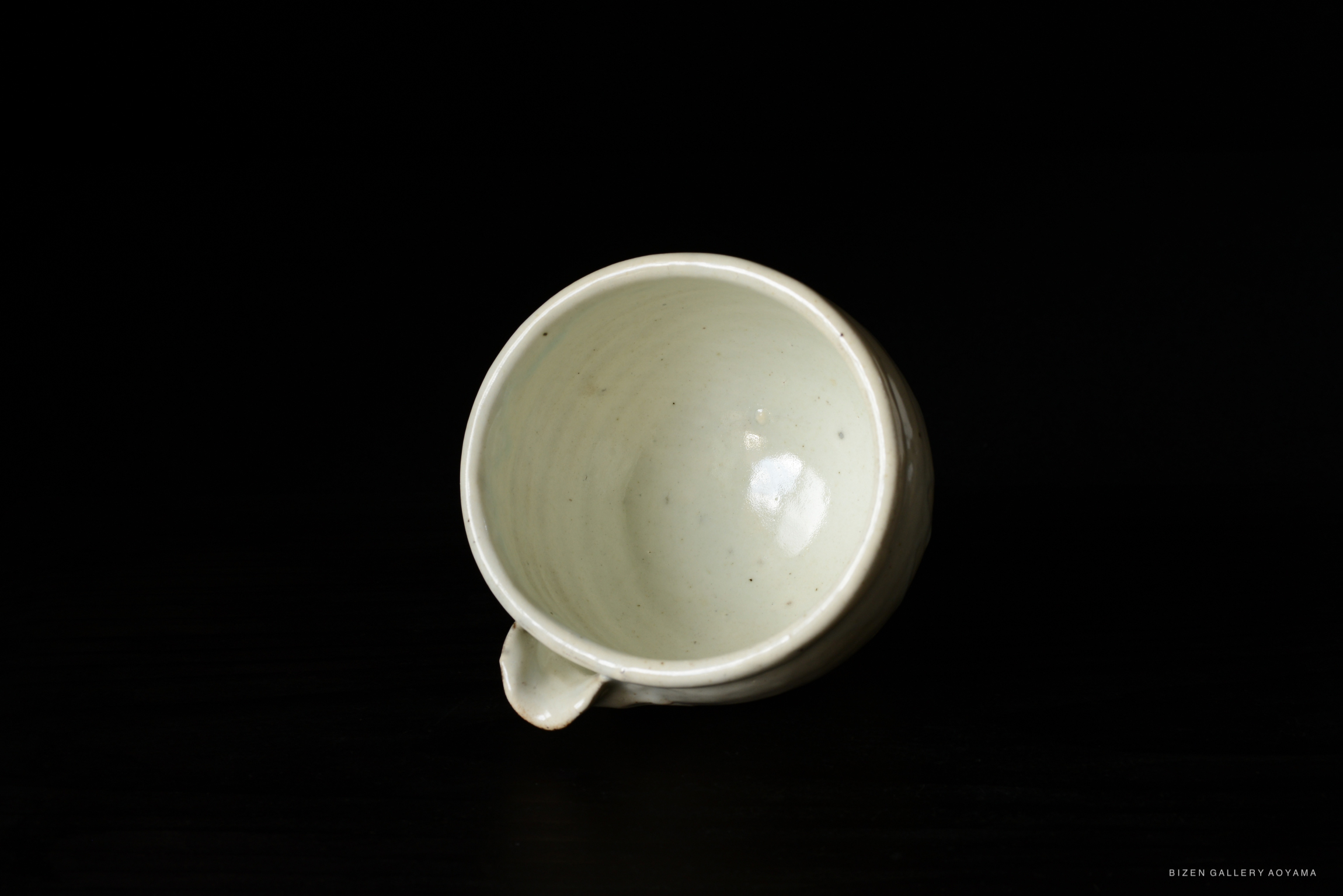 A close-up view of a light-colored ceramic cup with a handle, placed on a dark surface.