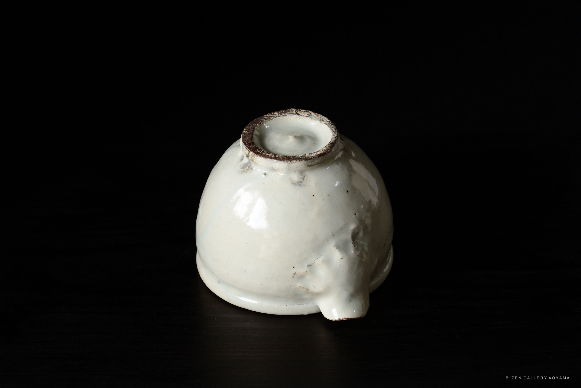 A uniquely shaped white pottery piece with a round base and an open top, featuring a textured surface and a rustic rim.