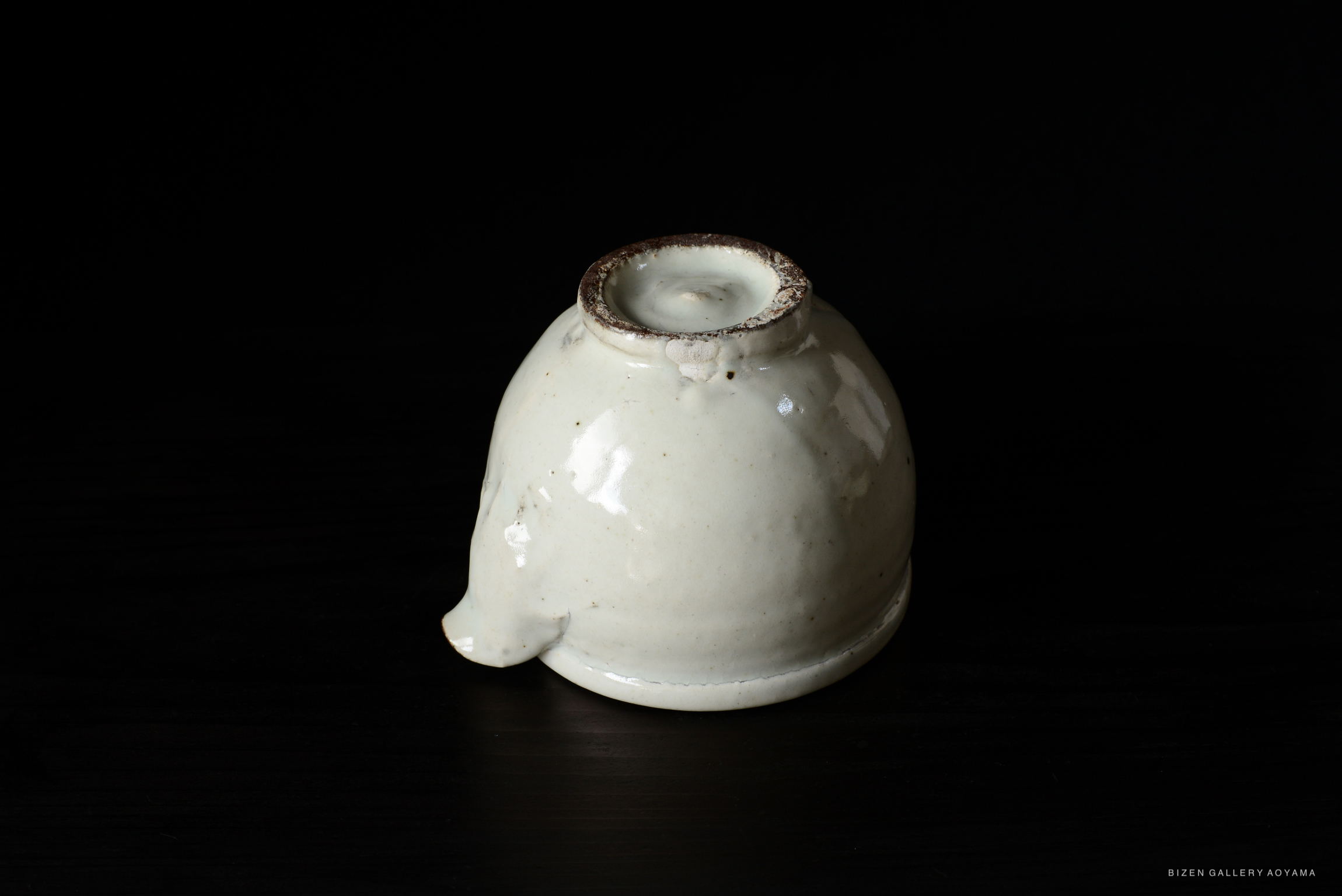 A white ceramic piece with a rounded shape and a small opening at the top, set against a black background.