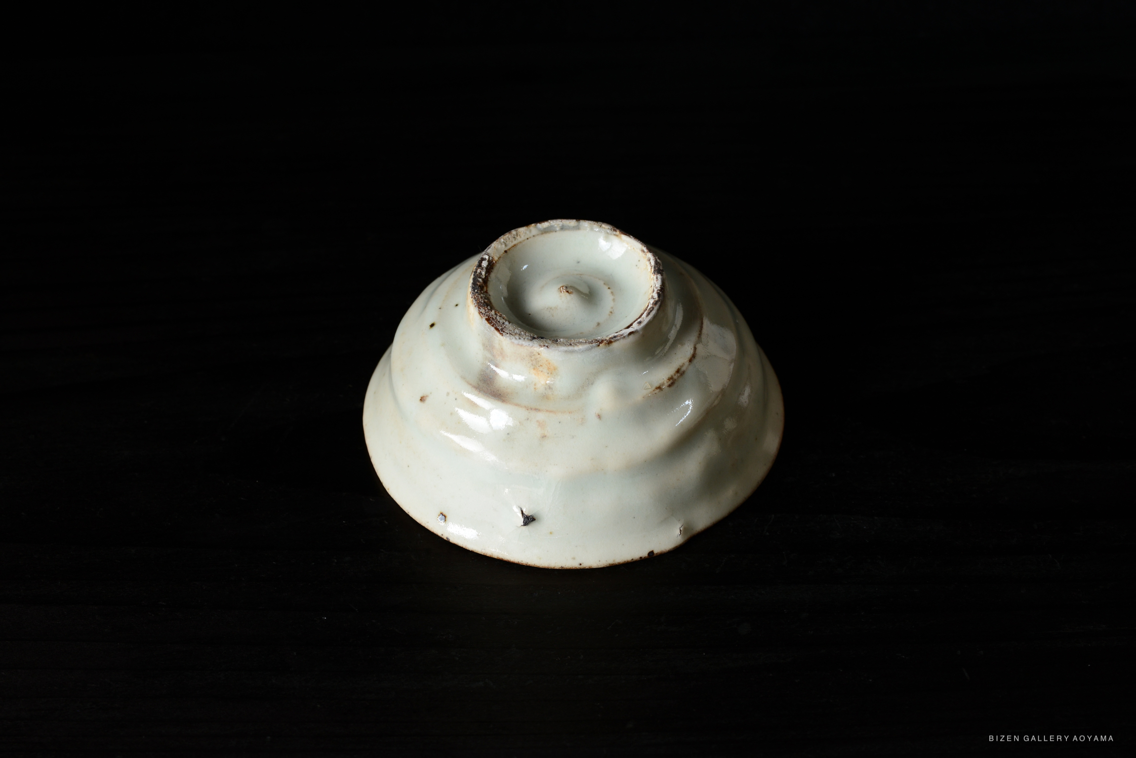Close-up of a round, white ceramic dish with a spiraled design, showcasing a simple and elegant aesthetic, placed on a dark surface.