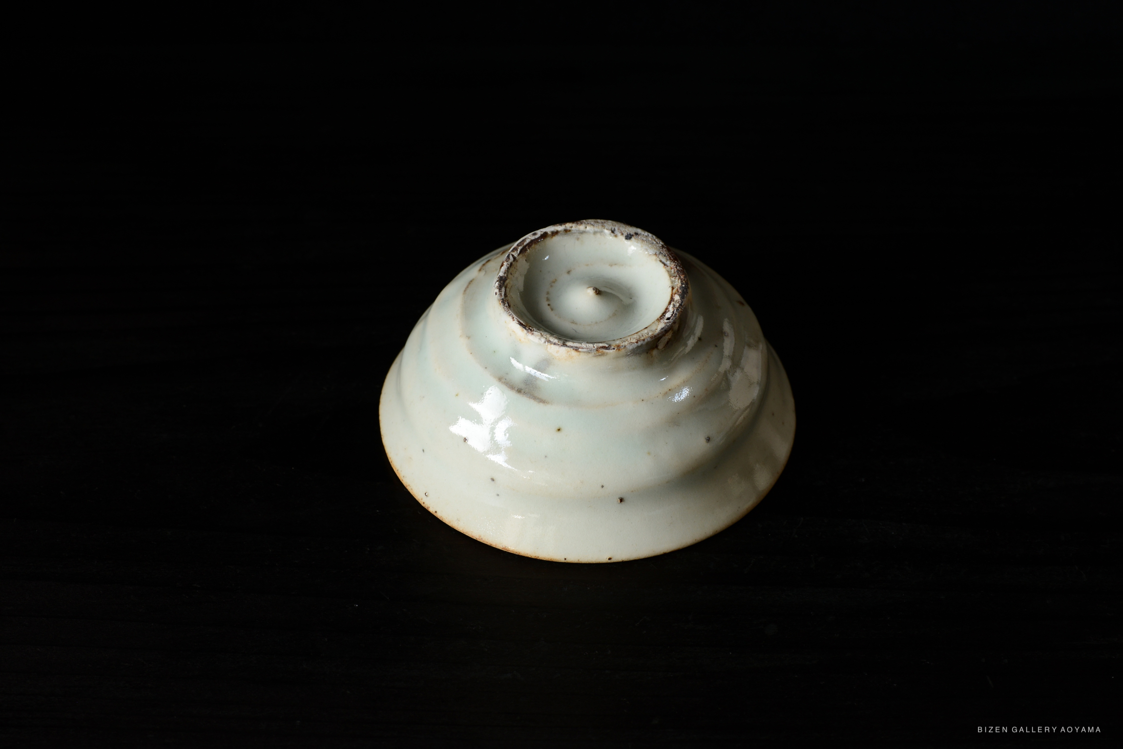 A close-up of a pale blue ceramic dish with a spiral design and a circular opening at the center, resting on a dark surface.
