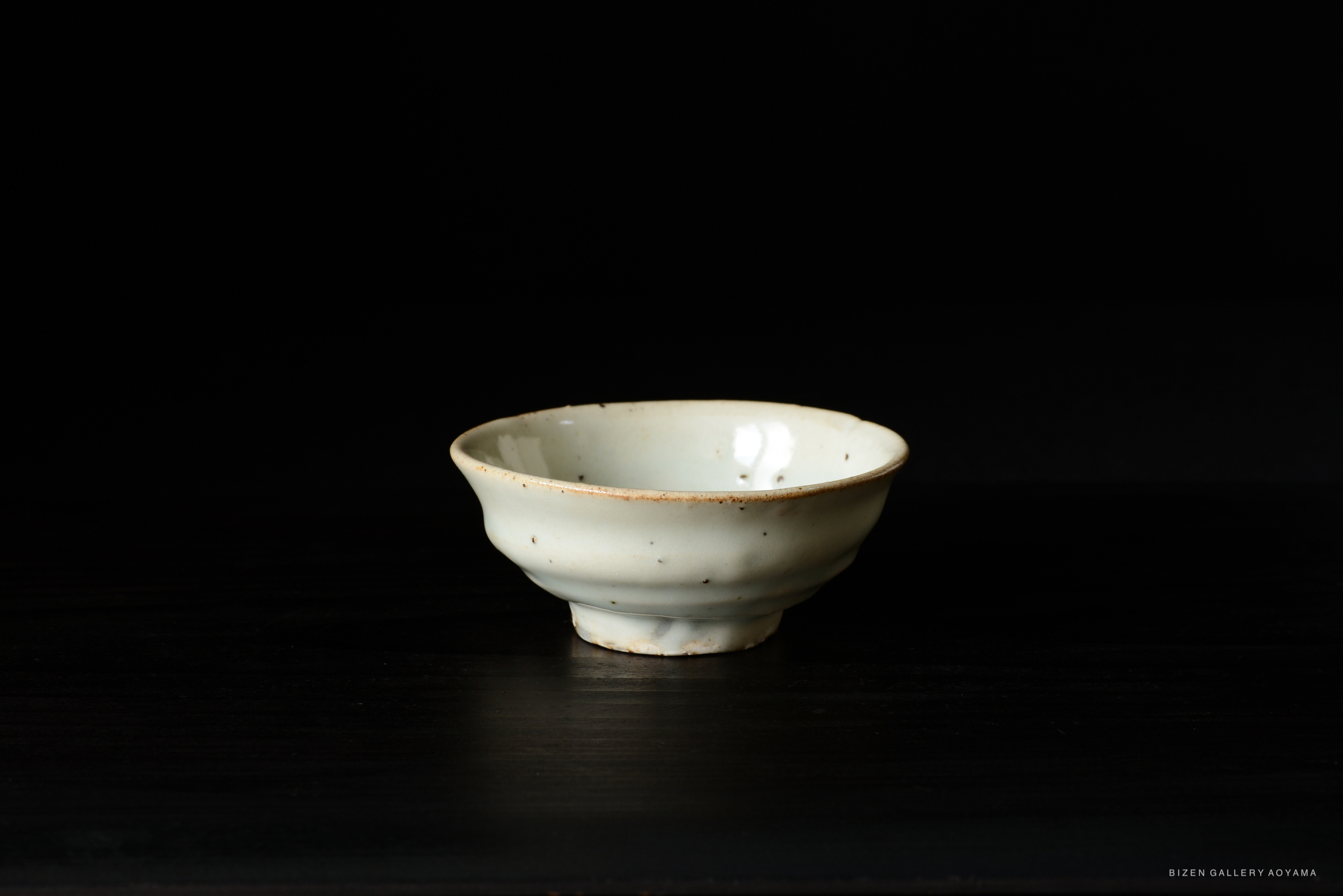 A ceramic bowl with a smooth, light-colored surface and a slightly flared rim, resting on a dark wooden surface.