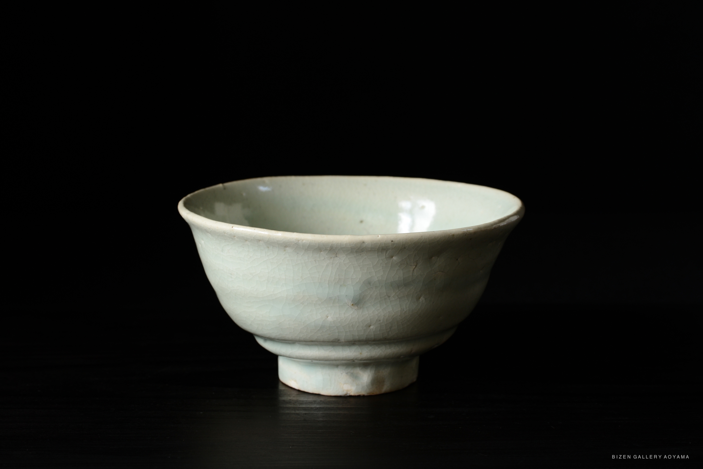 A light blue ceramic bowl with a smooth glaze and a shallow base, set against a dark background.