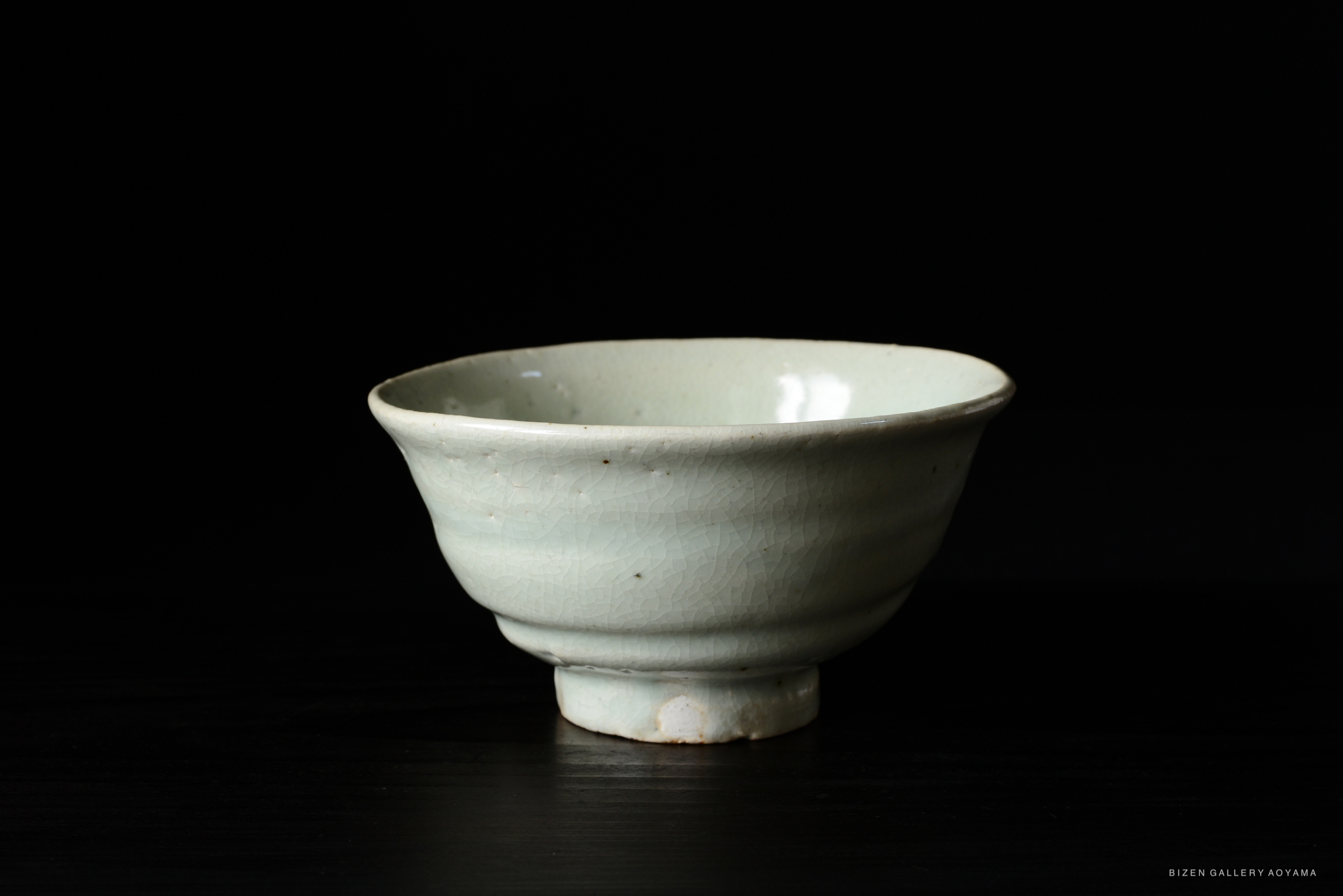 A light green ceramic bowl with a slightly flared rim and a short foot, set against a black background.