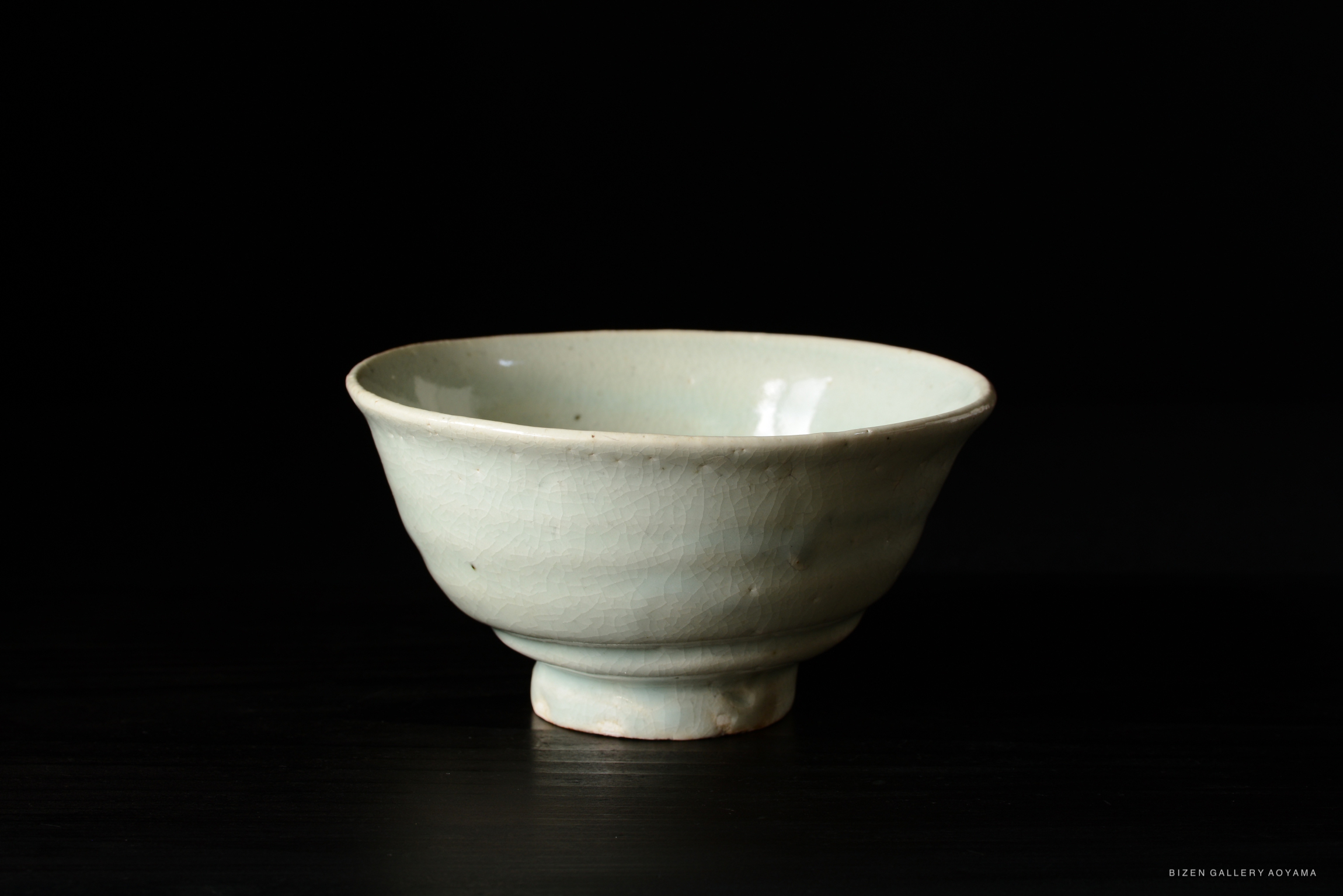 A light green Bizen pottery bowl with a smooth surface and a round base, captured against a dark background.