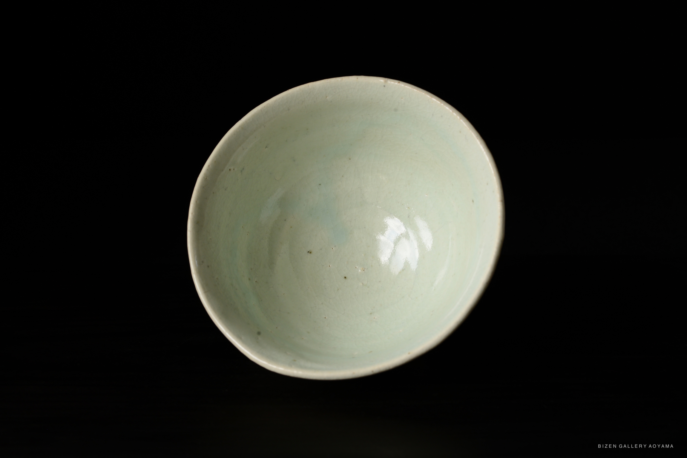 A close-up view of a light green ceramic bowl, displaying a smooth, glossy interior and a slightly textured rim, set against a black background.