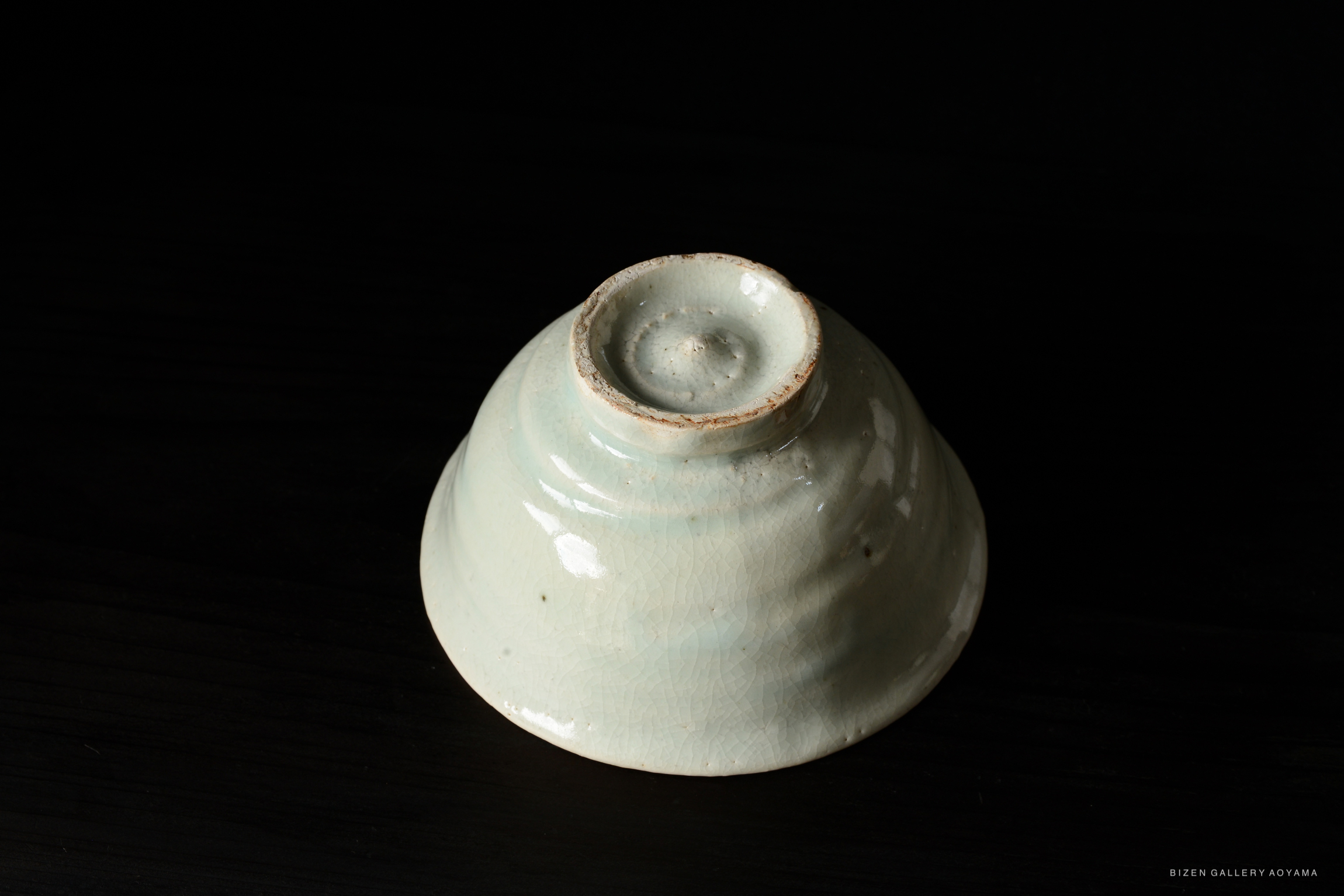 A close-up view of a traditional ceramic bowl with a glossy pale blue glaze, displayed on a dark surface.