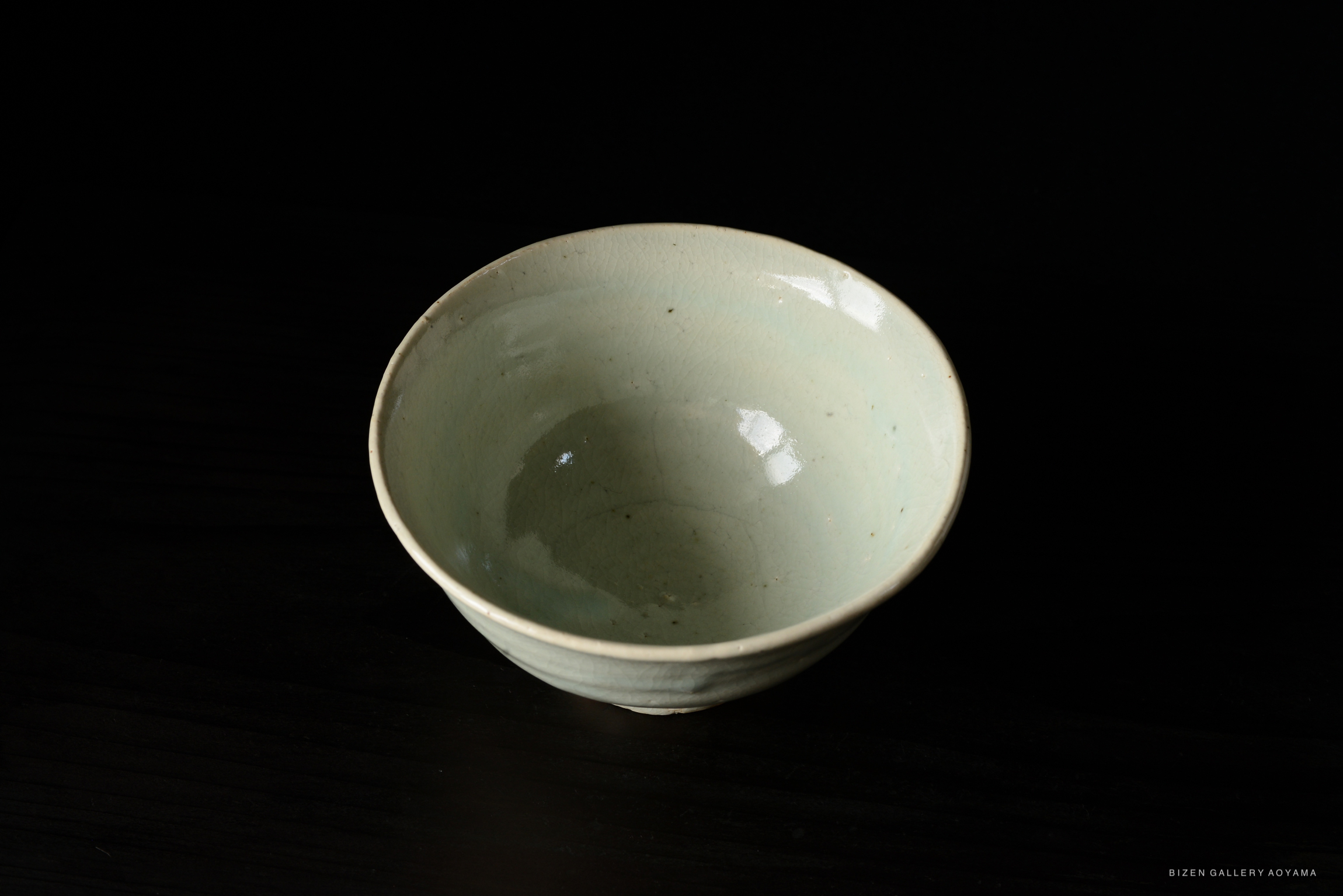 A simple, pale green ceramic bowl with a smooth interior and slightly textured exterior, set against a black background.