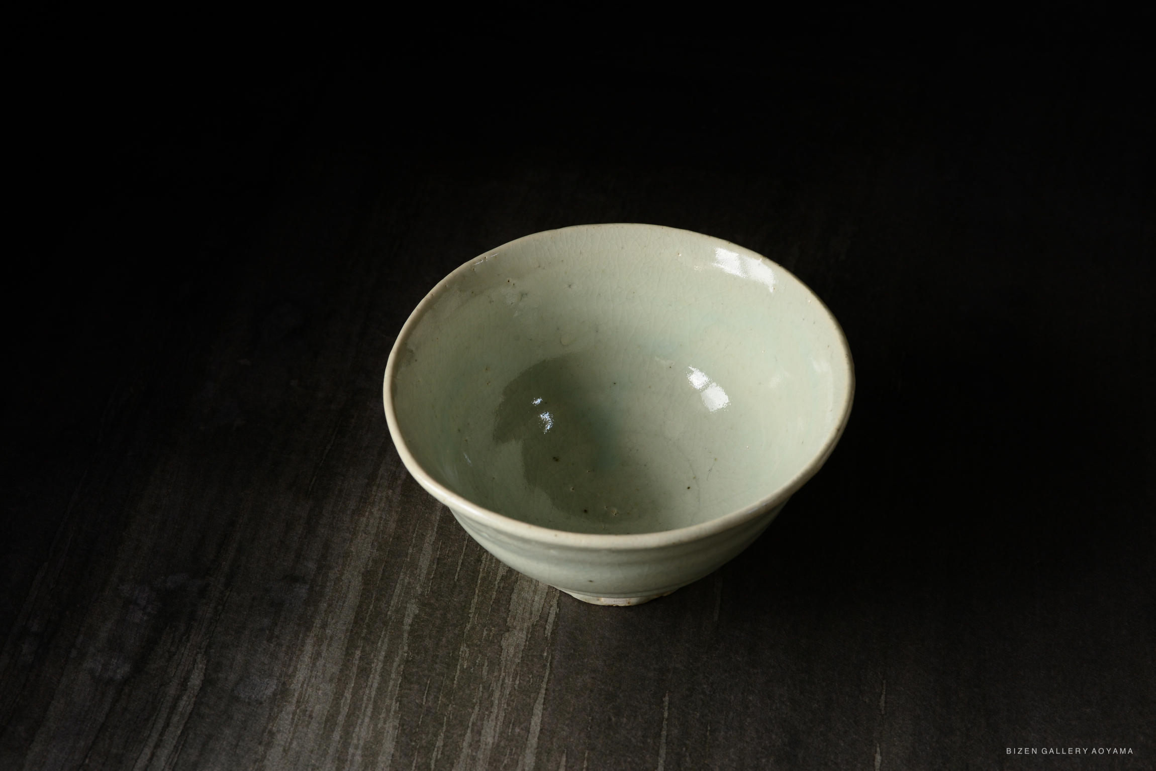 A simple, light green ceramic bowl with a smooth finish, set against a dark background.