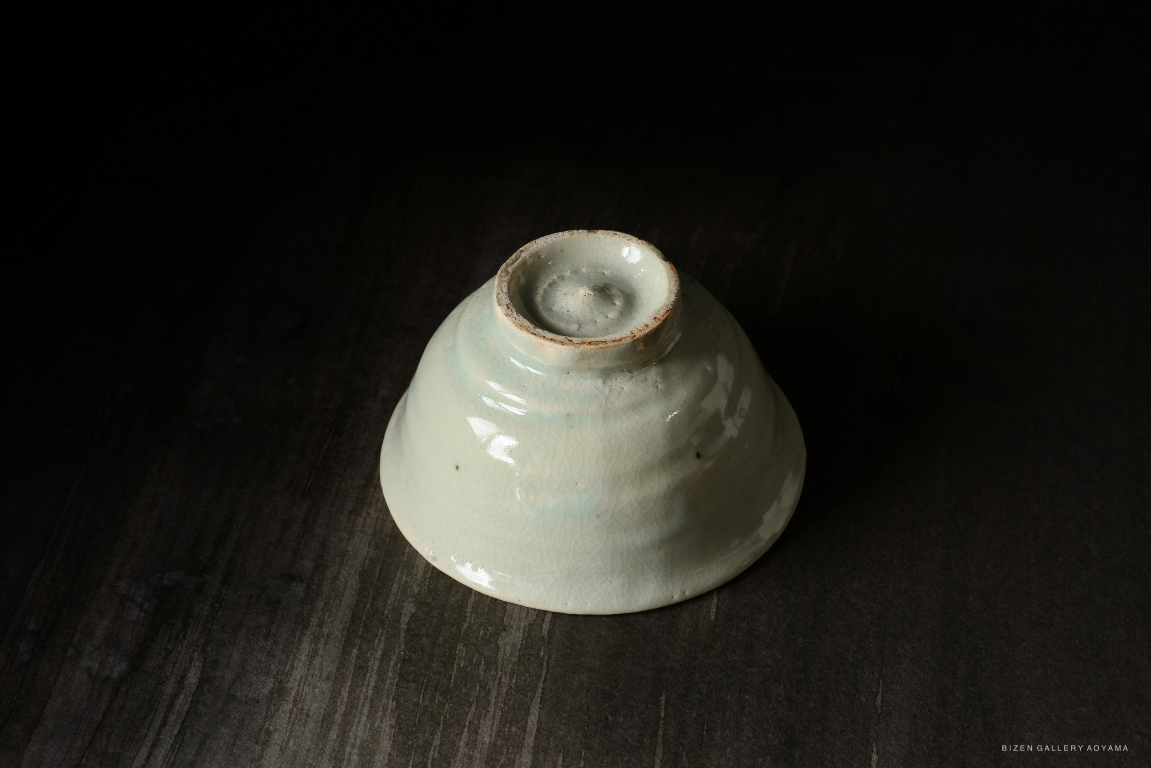 A ceramic bowl with a glossy, pale blue glaze, featuring a slightly flared rim and a smooth surface, positioned against a dark background.