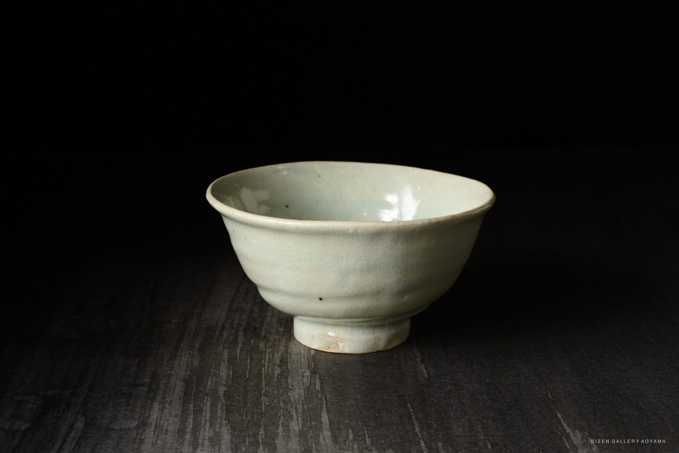A light blue ceramic bowl with a slightly raised base, showcasing a smooth surface and subtle cracks, set against a dark background.