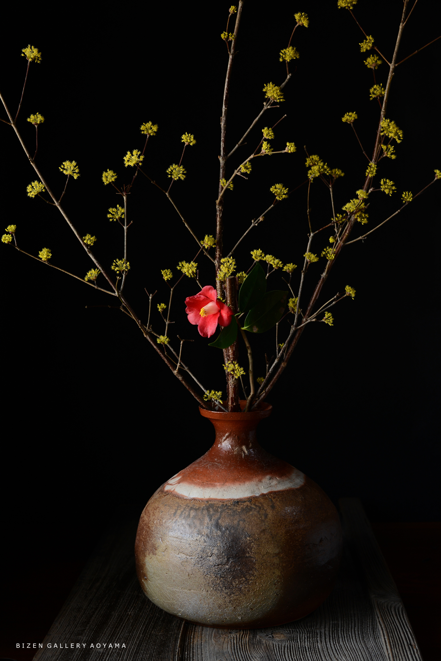 陶器の花瓶に、黄色い花と赤い花が飾られた生け花のアレンジメント