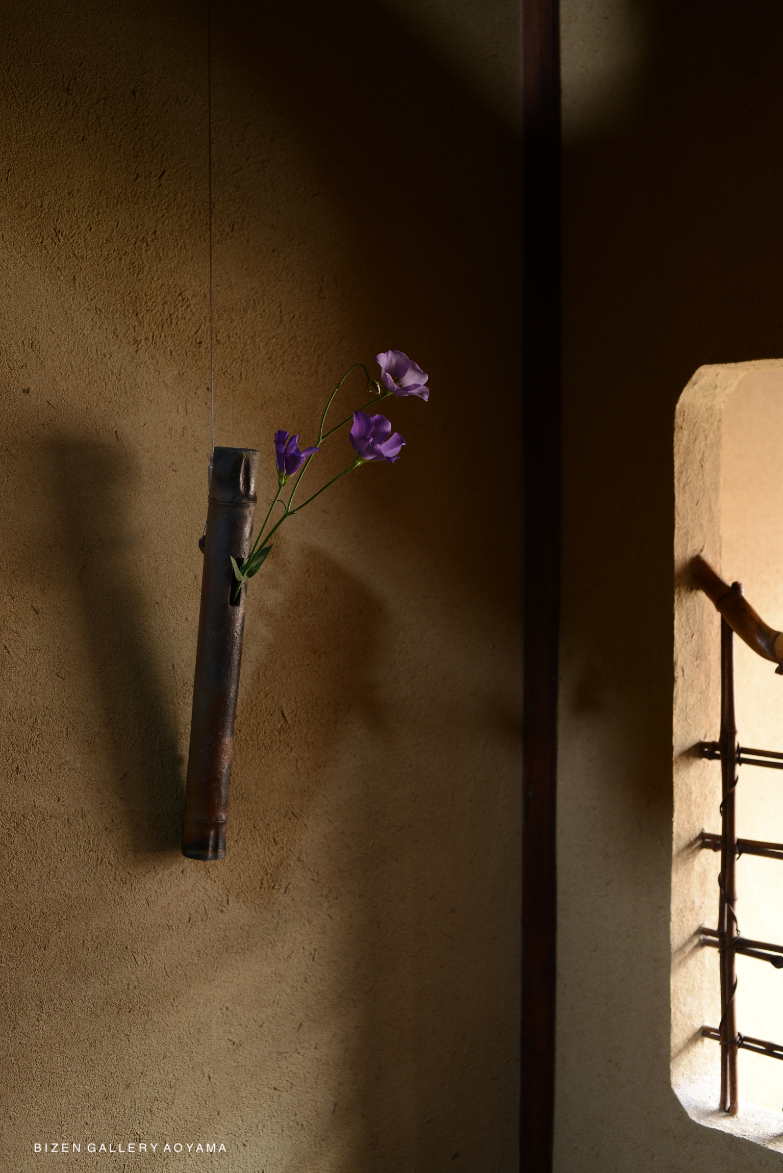 A bamboo vase hanging on a wall, featuring purple flowers, with a soft background of earthy tones.