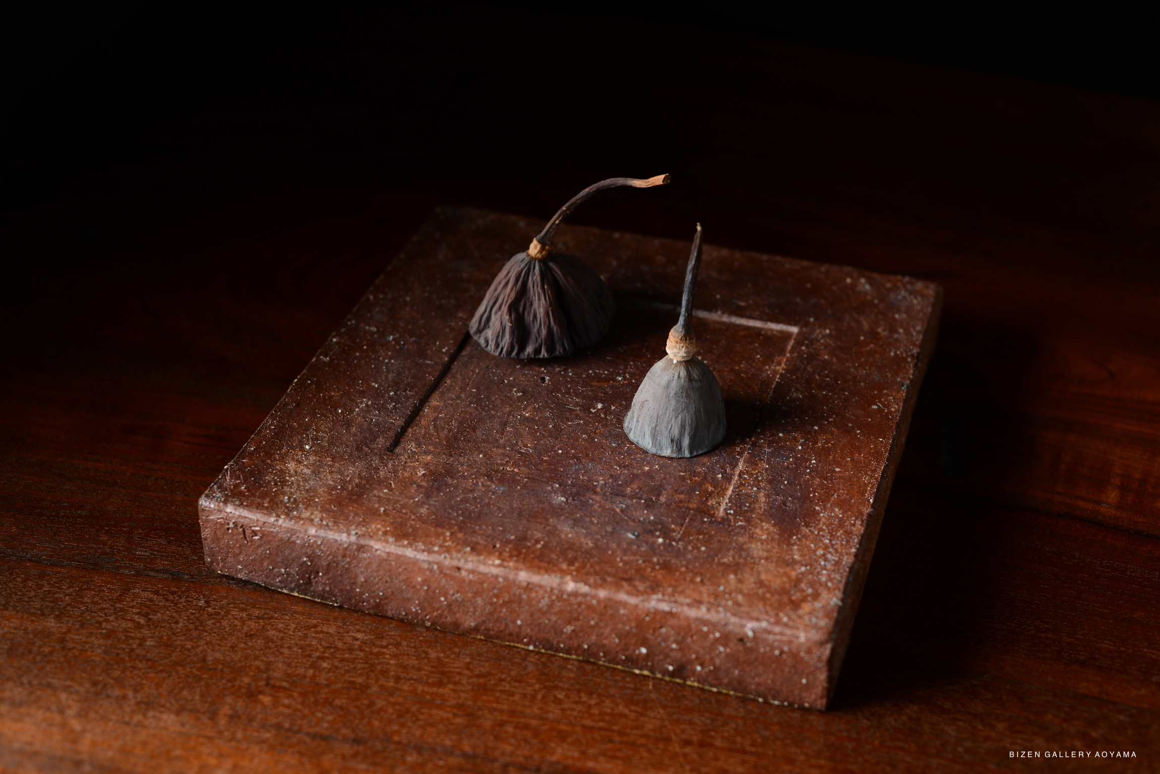 Artistic still life featuring two small decorative objects resembling mountains, placed on a rustic brown square base.