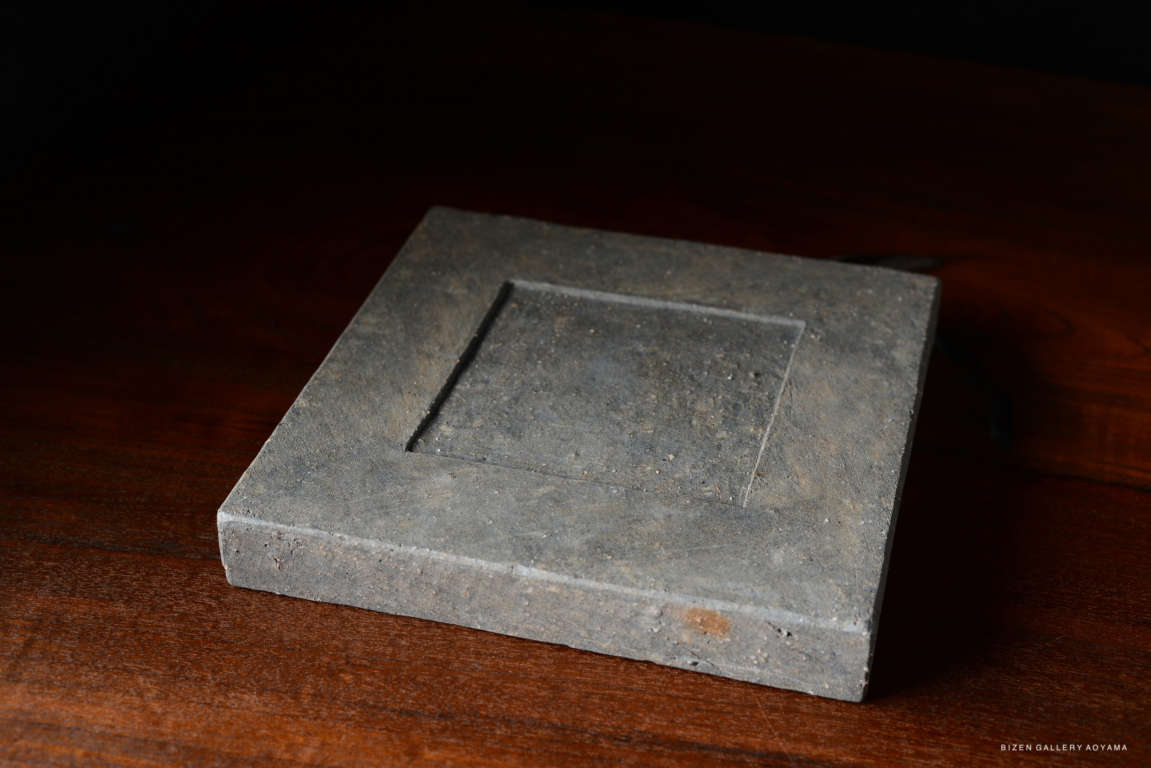 A stylish square plate made of textured gray material, placed on a wooden surface.